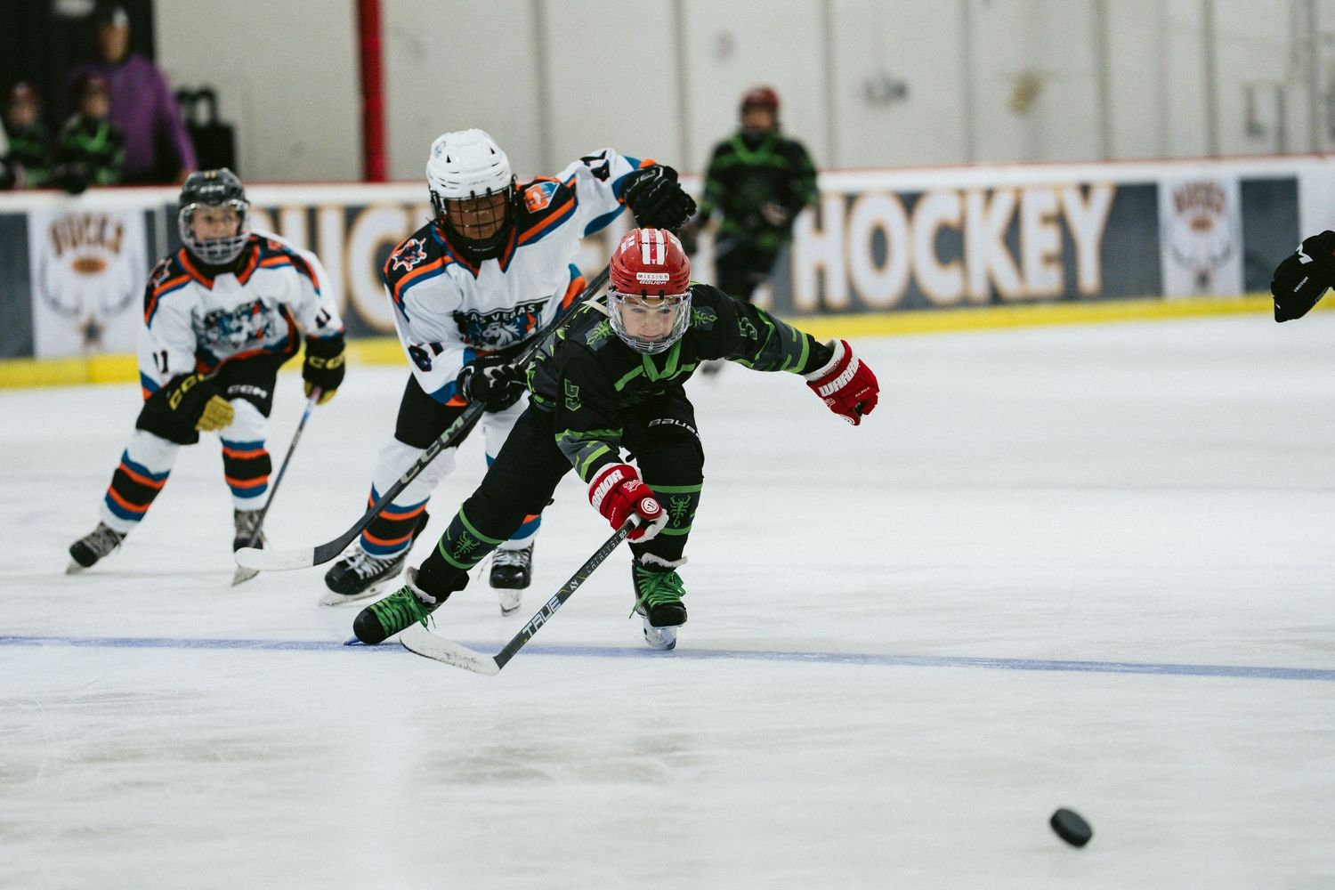 Young hockey players race for the puck during a competitive youth ice hockey game indoors.