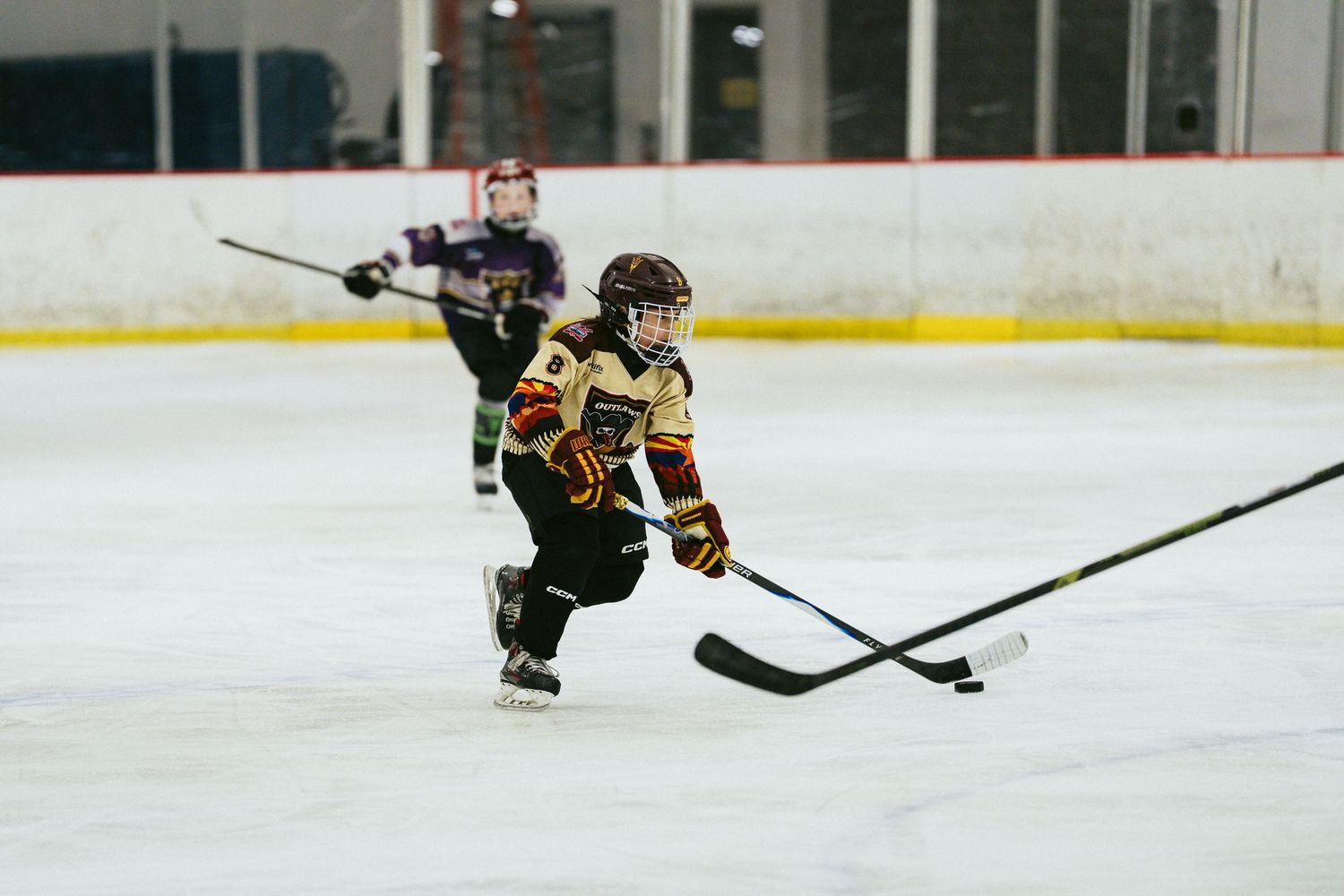 Young hockey player skates with the puck during a youth ice hockey game on indoor rink.