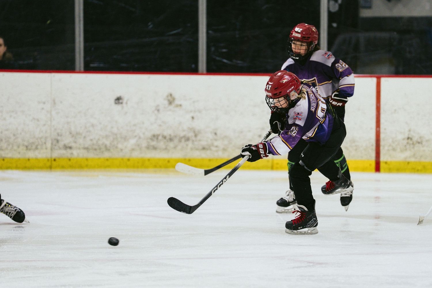 Young hockey player shoots the puck during a youth ice hockey game on an indoor rink.