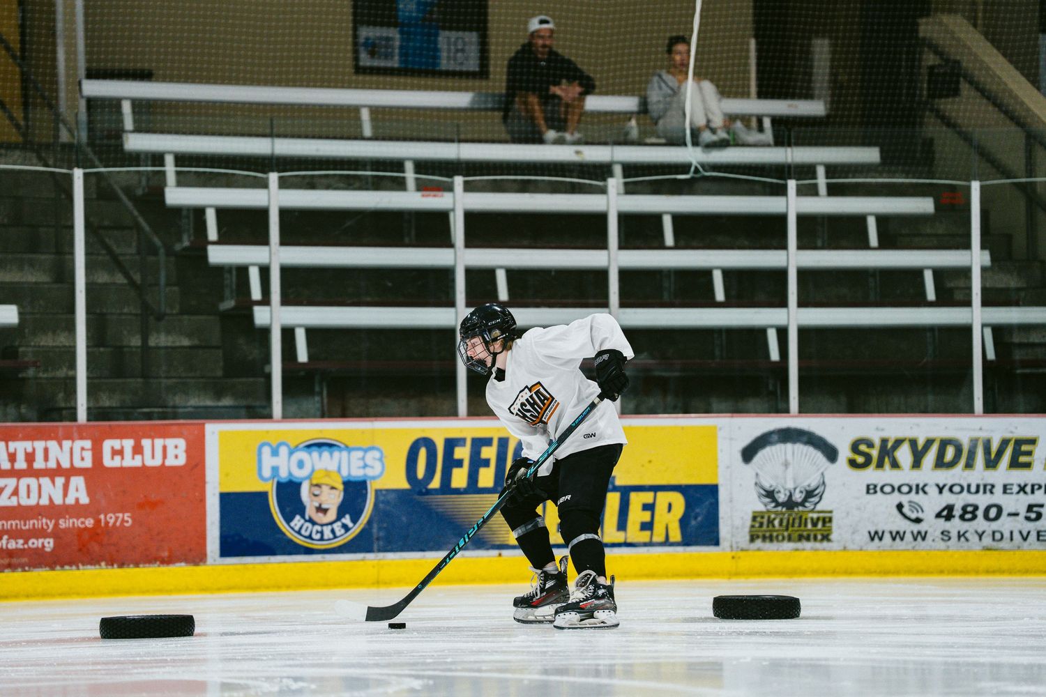 Hockey player in black and white uniform handles puck on ice at arena with Skydive sponsor banner.