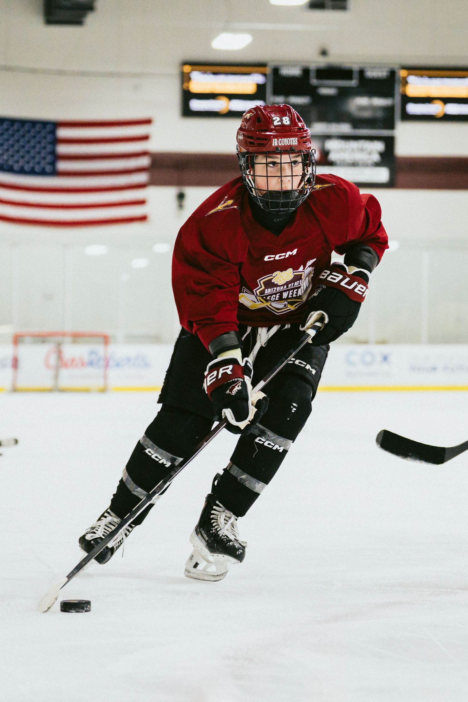 Young hockey player in red CCM jersey number 28 skating with puck during ice hockey practice at indoor rink.
