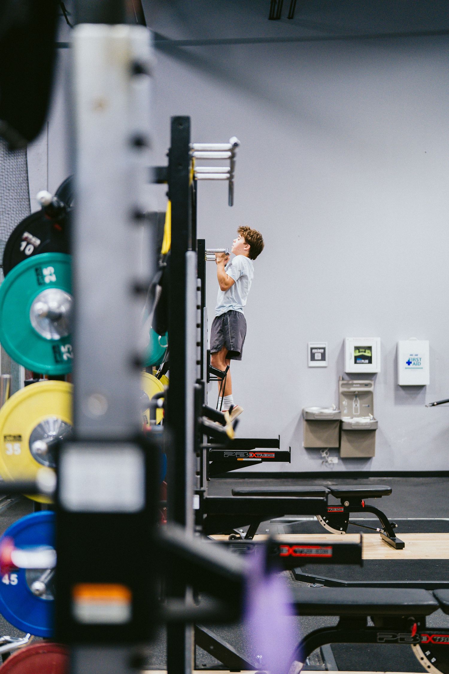 Young athlete doing pull-ups on a squat rack in a well-equipped weight room with bumper plates.