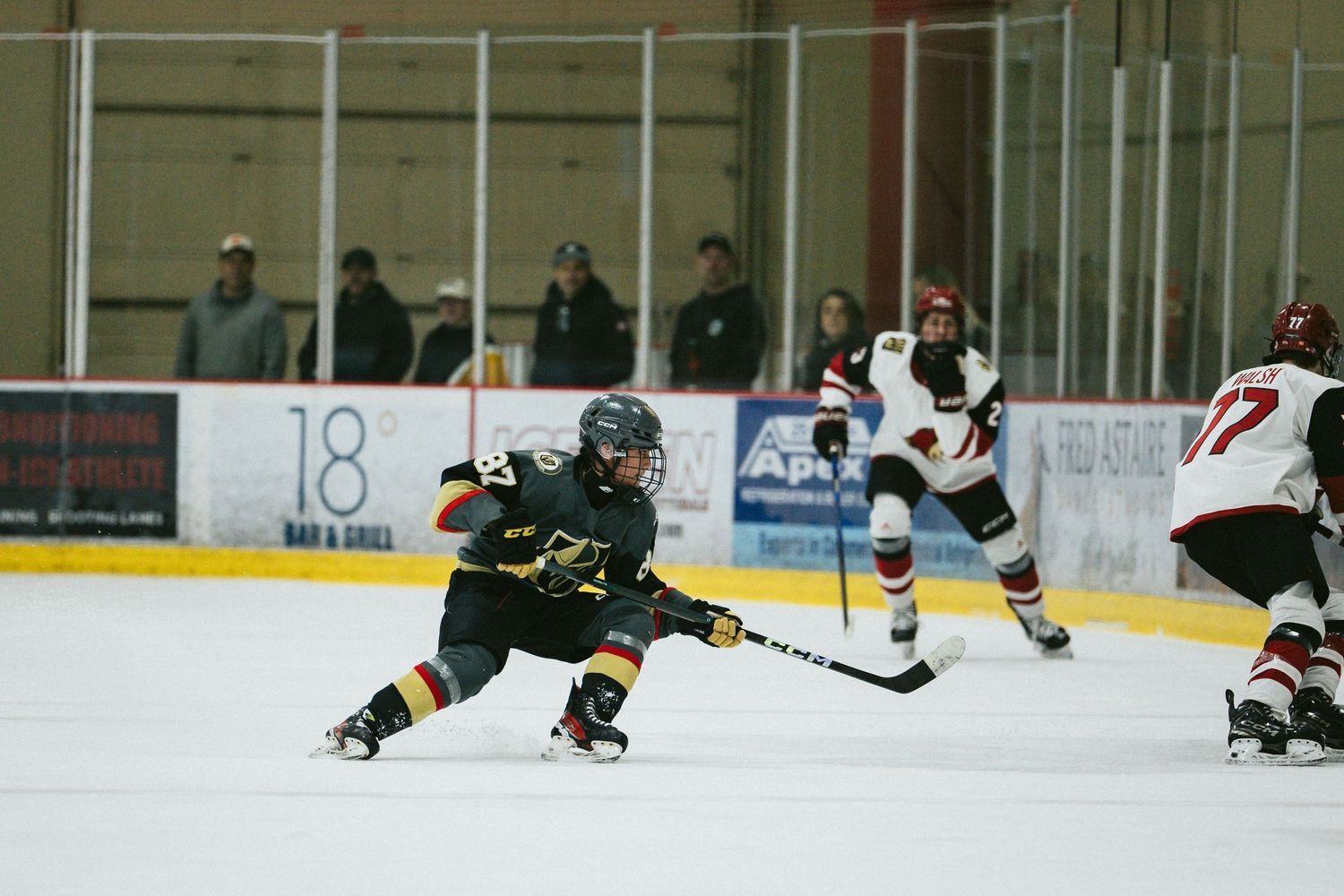 Youth hockey game action with players in black and white uniforms competing for the puck.