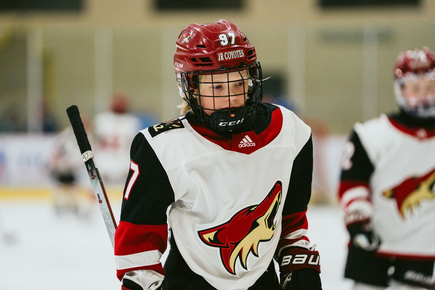 Hockey players in red and white uniforms skate during an indoor game.