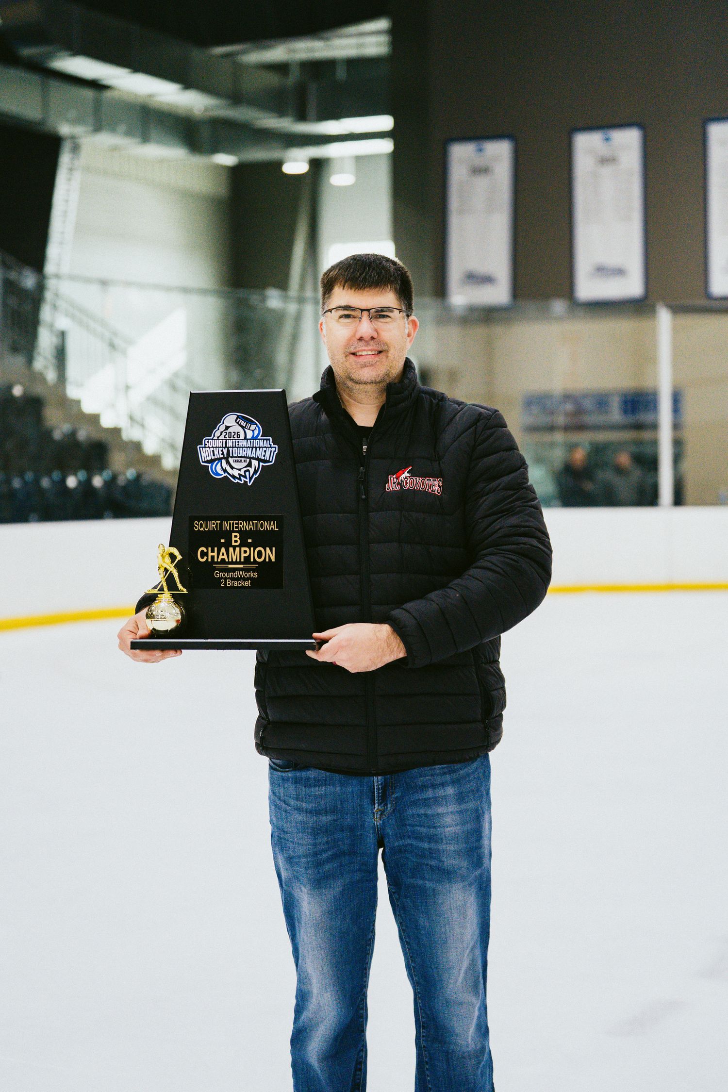 Person in black jacket holding championship award on ice rink.