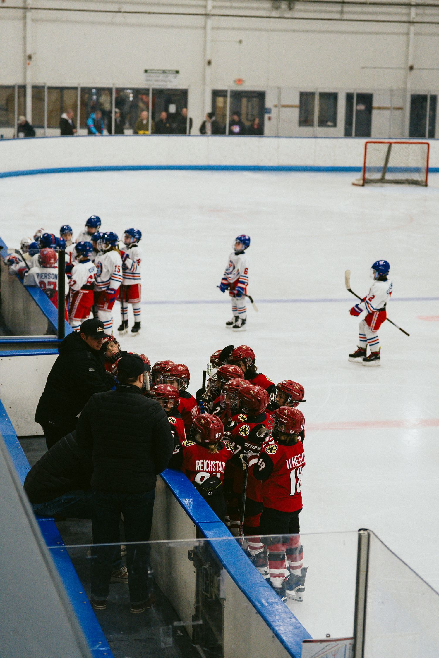 Hockey team lines up along the boards while coaches provide instruction during practice.