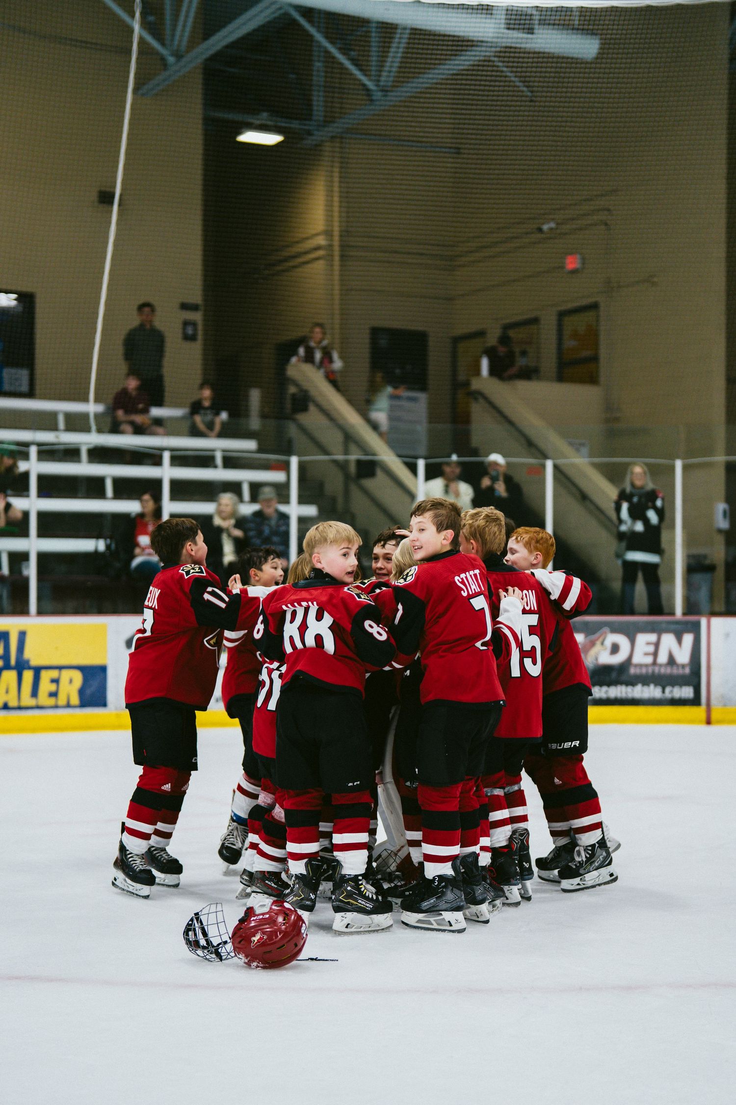 Youth hockey team in red jerseys huddles together on ice celebrating after a game at indoor rink.
