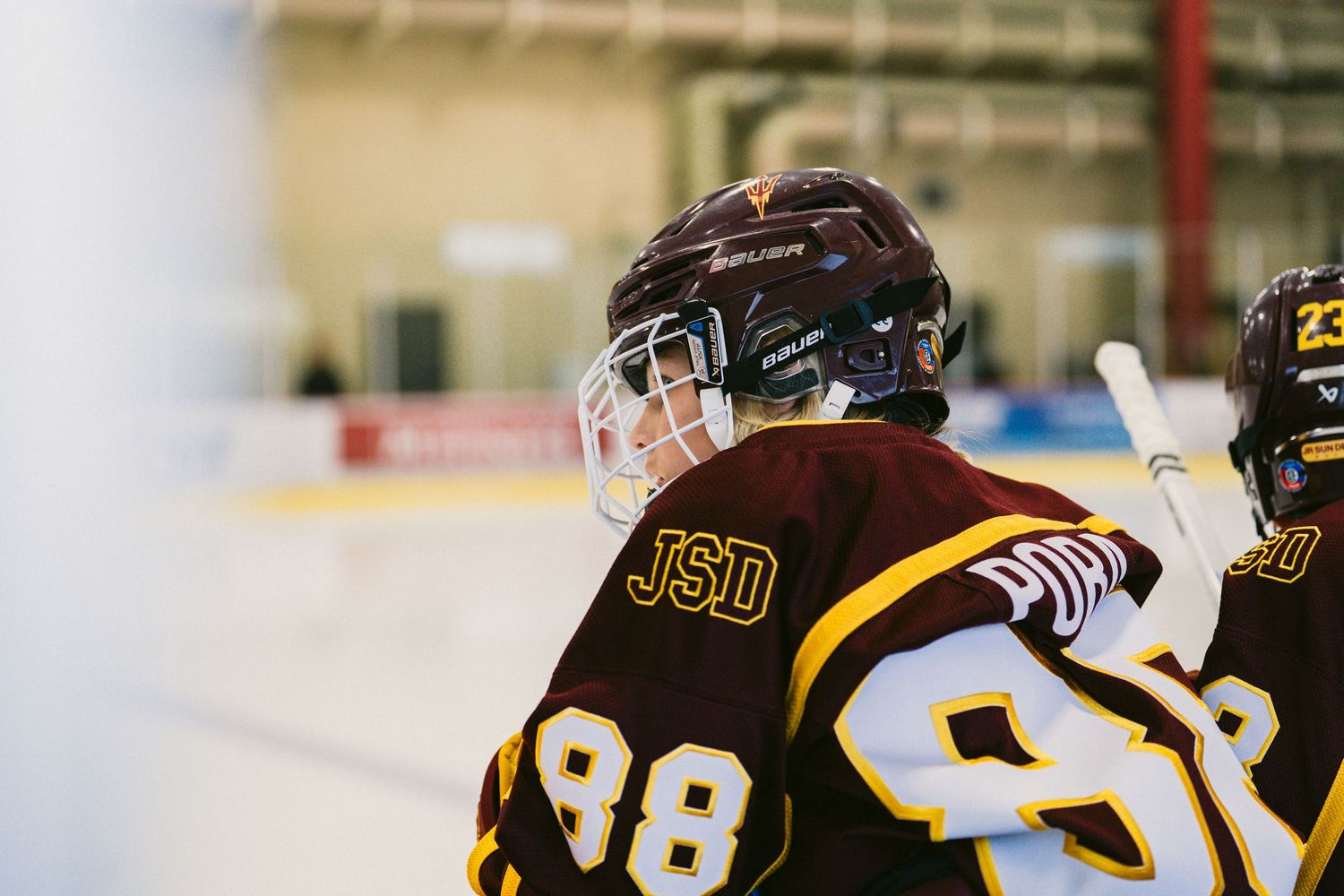 Hockey players in black and gold uniforms compete on an ice rink with advertising boards visible in the background.
