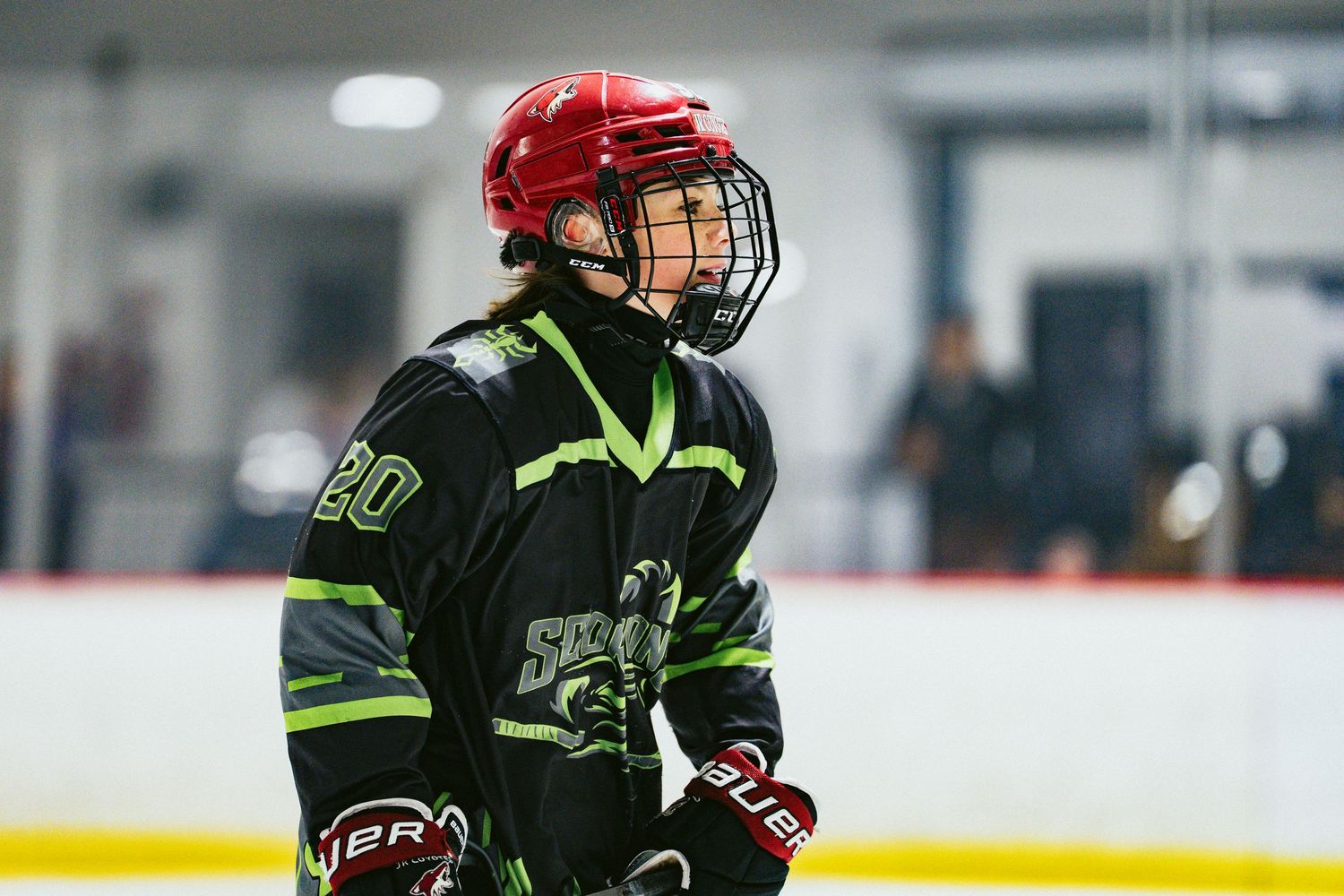 Young hockey player wearing number 20 in black and green uniform with red helmet stands on ice rink.