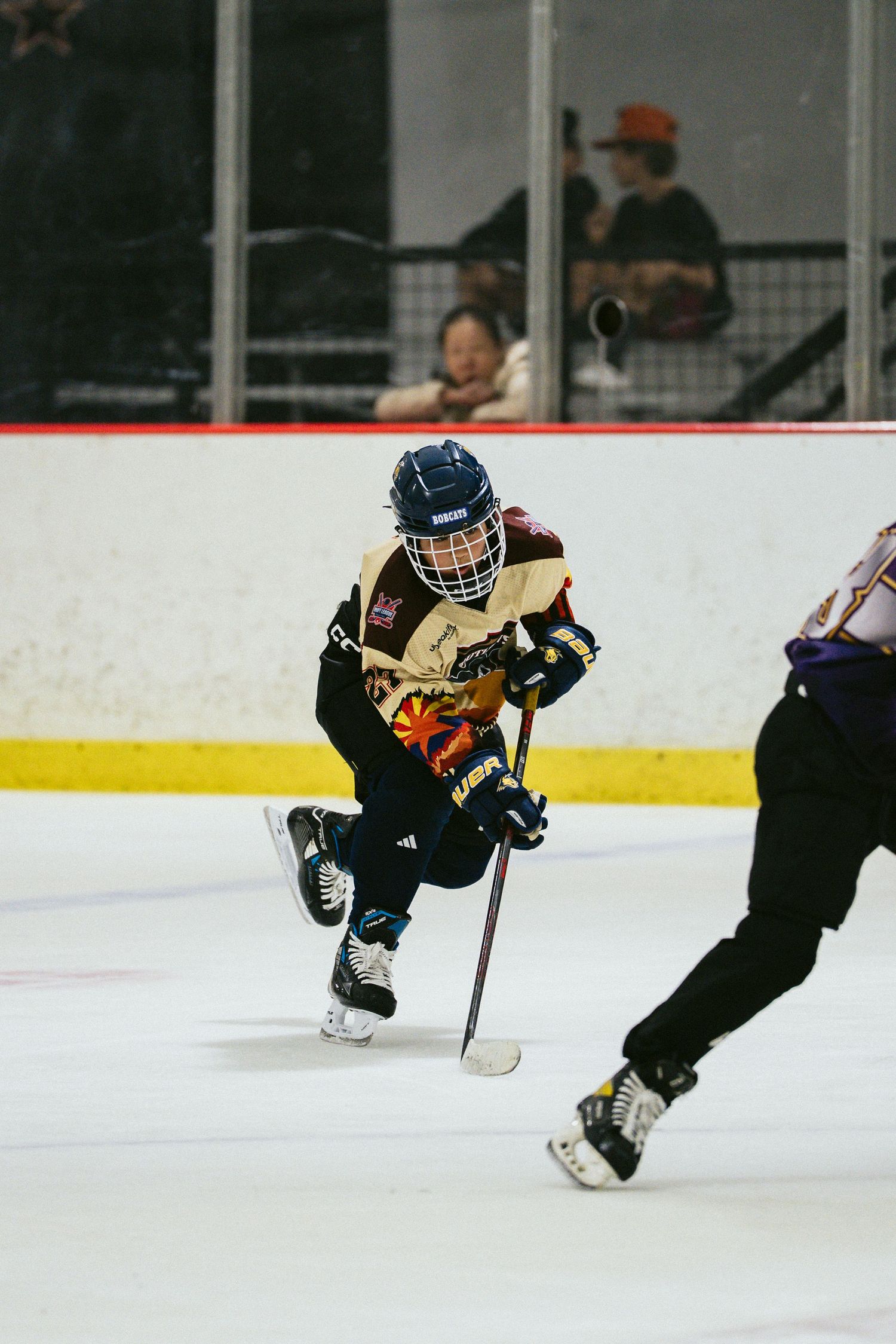 Young ice hockey player in colorful jersey skating with stick during a youth hockey game at an indoor rink.
