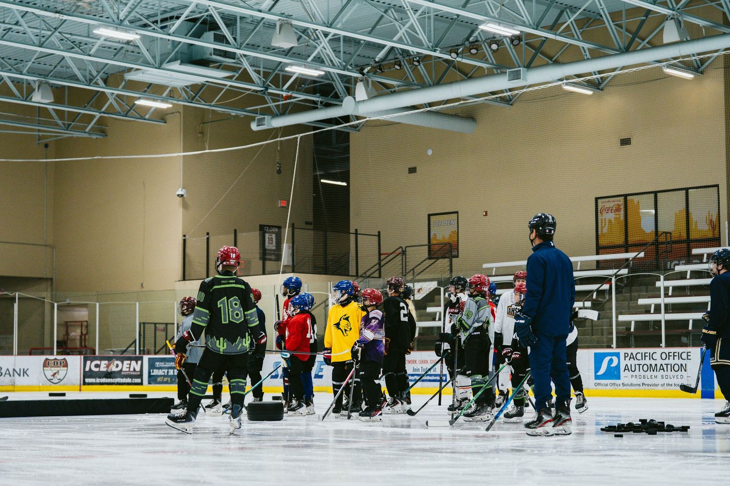 Youth hockey players receive on-ice coaching instruction during a practice session at an indoor ice rink.
