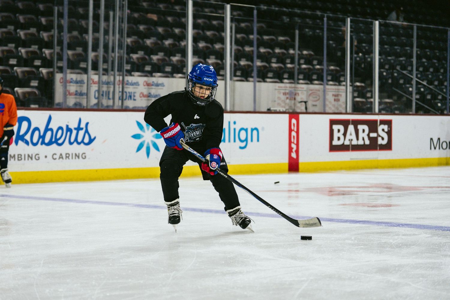 Youth hockey player in blue helmet skates with the puck during an indoor ice hockey training session.