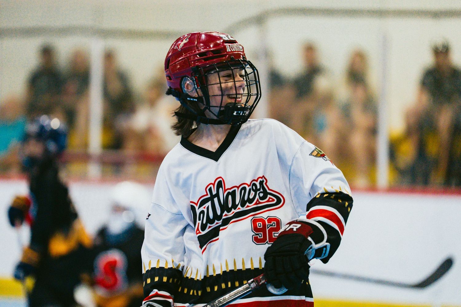 Hockey player wearing number 52 in a white Stallions jersey and red helmet stands on the ice rink.