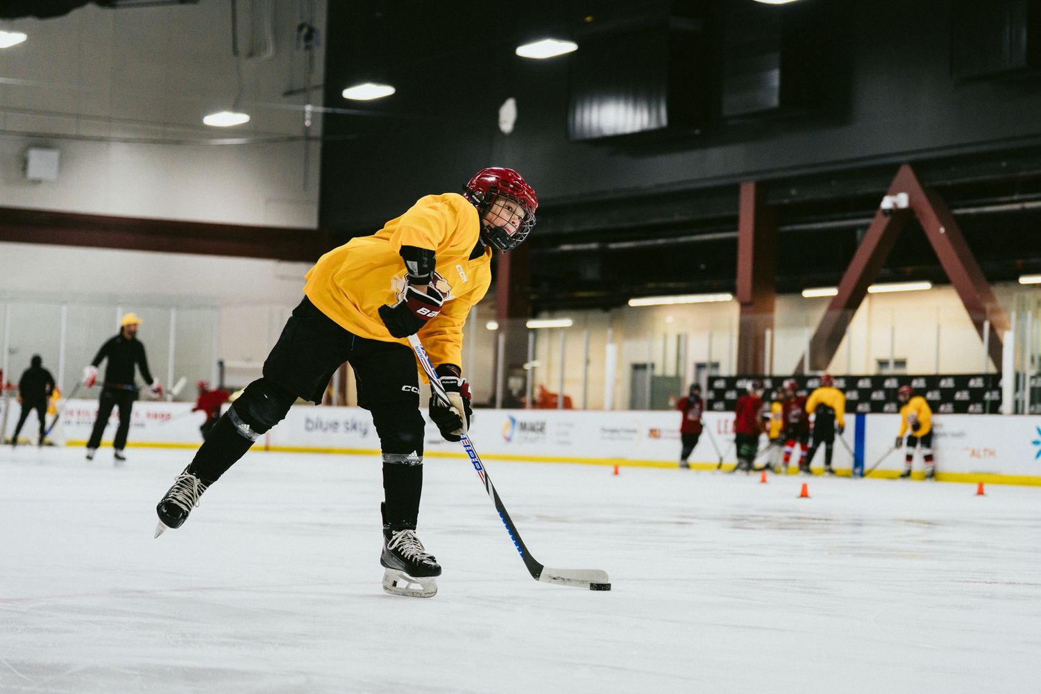 Young hockey player in yellow jersey takes a shot on ice during indoor hockey practice session.