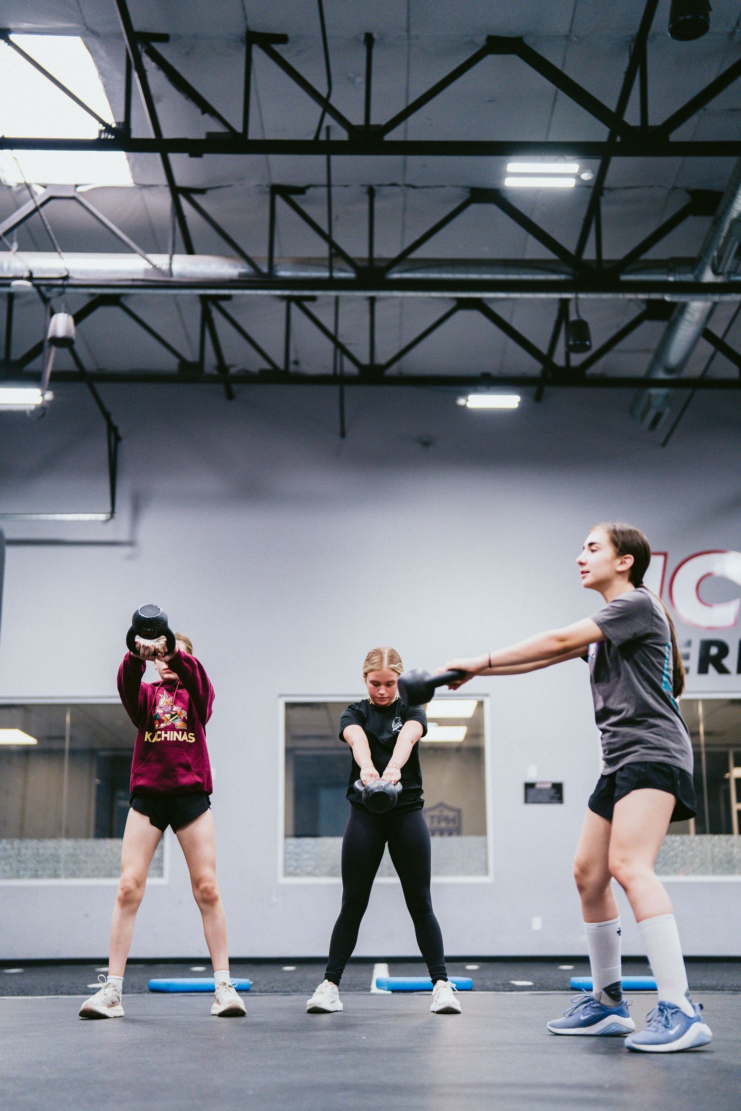 Three women exercising in a gym, practicing fitness moves on a studio floor with mirrors in the background.