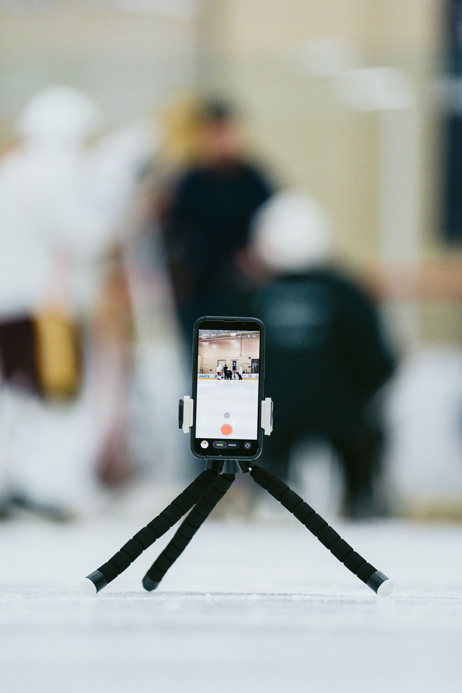 A smartphone mounted on a flexible mini tripod records a hockey practice session at an indoor ice rink.