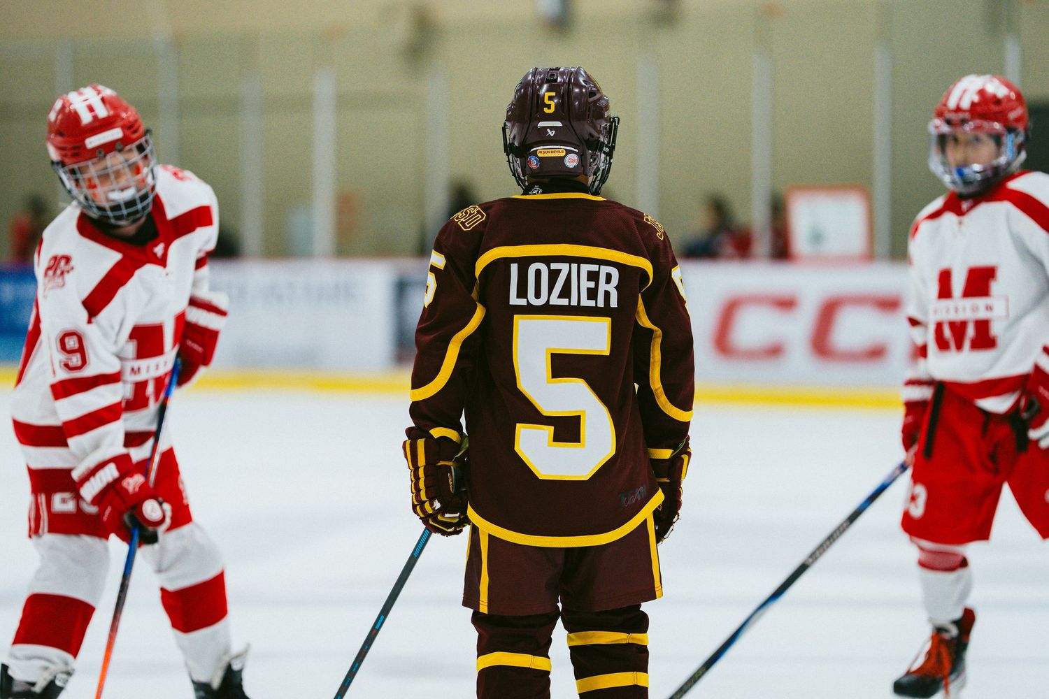 Youth hockey players in red and brown jerseys face off during an ice hockey match.