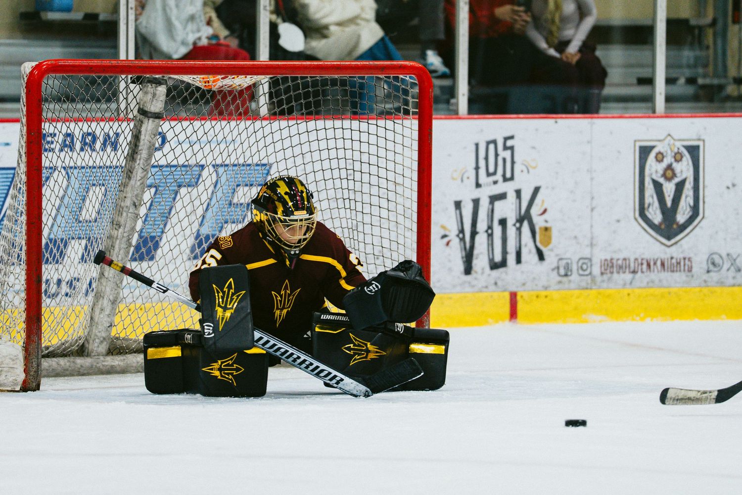 Hockey goalie defends the net as players battle for the puck near the goal.