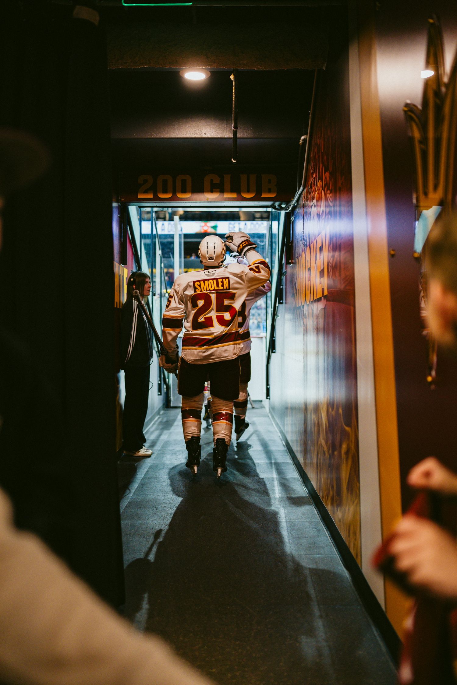 Hockey player walks through dimly lit arena tunnel before game.