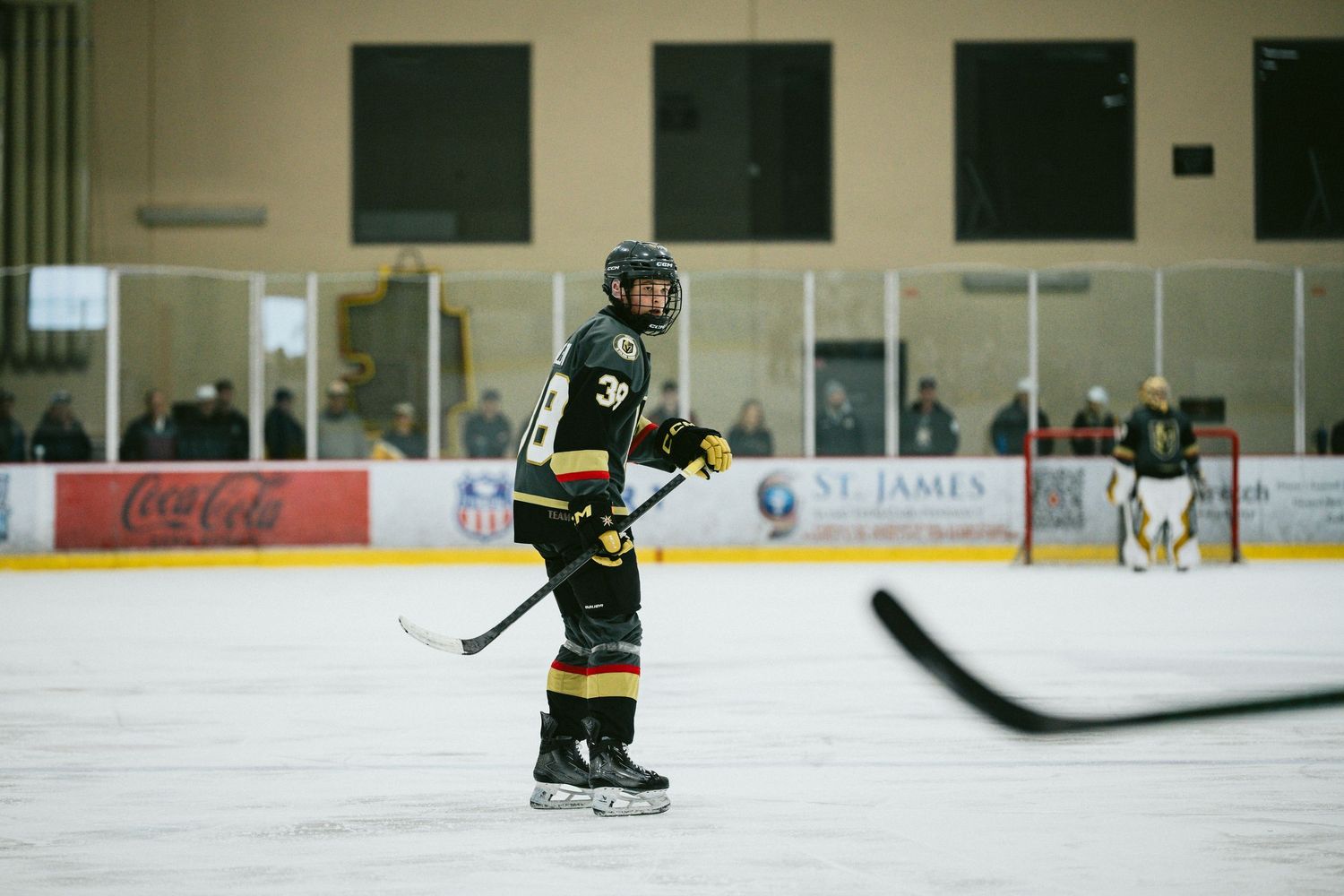 Hockey player in black and gold uniform stands ready on the ice during gameplay.