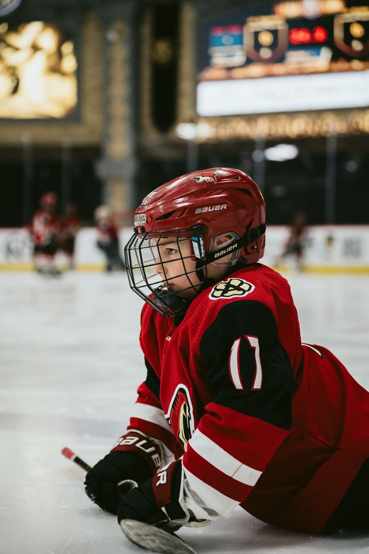 Hockey players in red jerseys and protective gear rest on the ice during a game break.