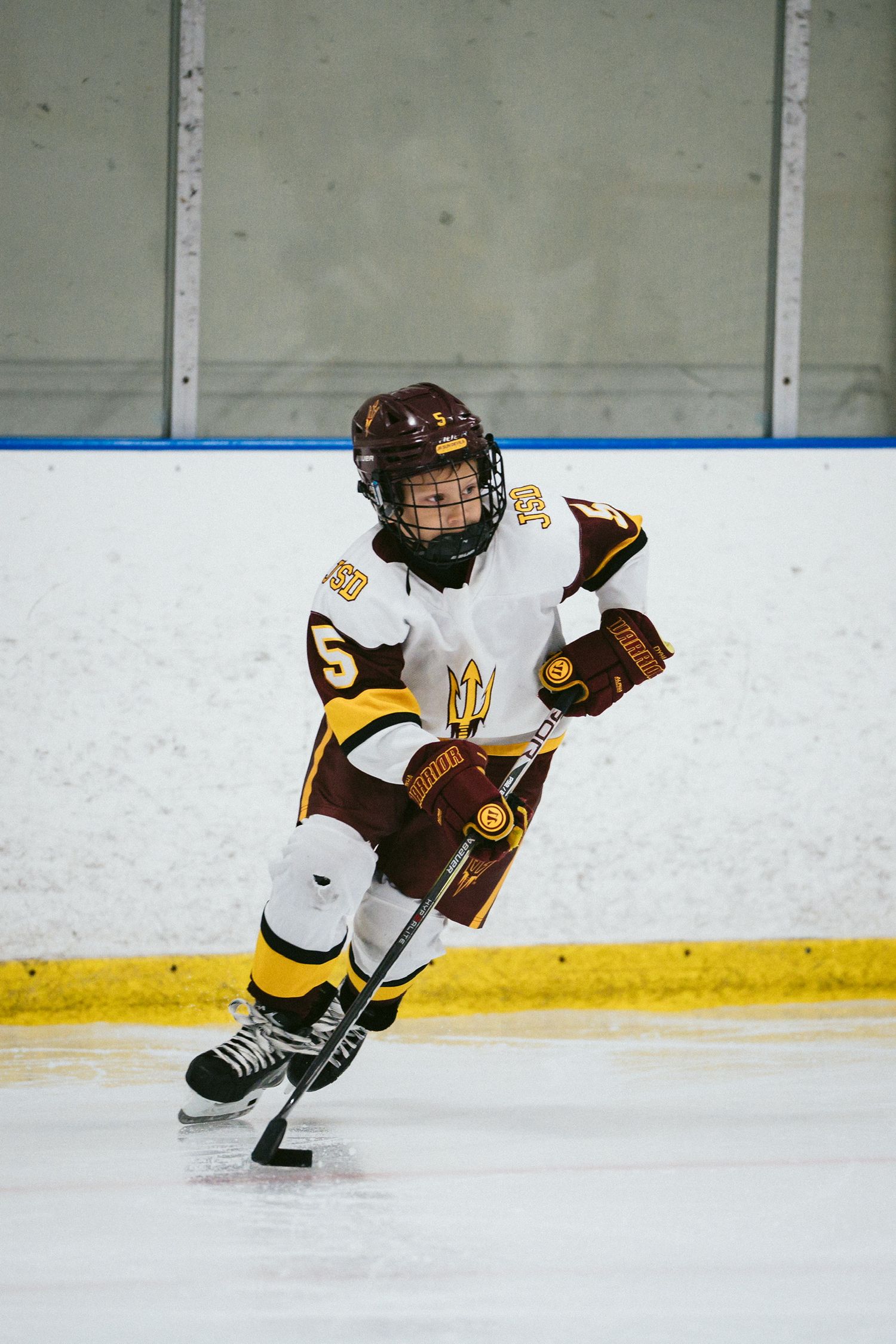 Youth hockey player in brown and yellow uniform skates with determination on ice.