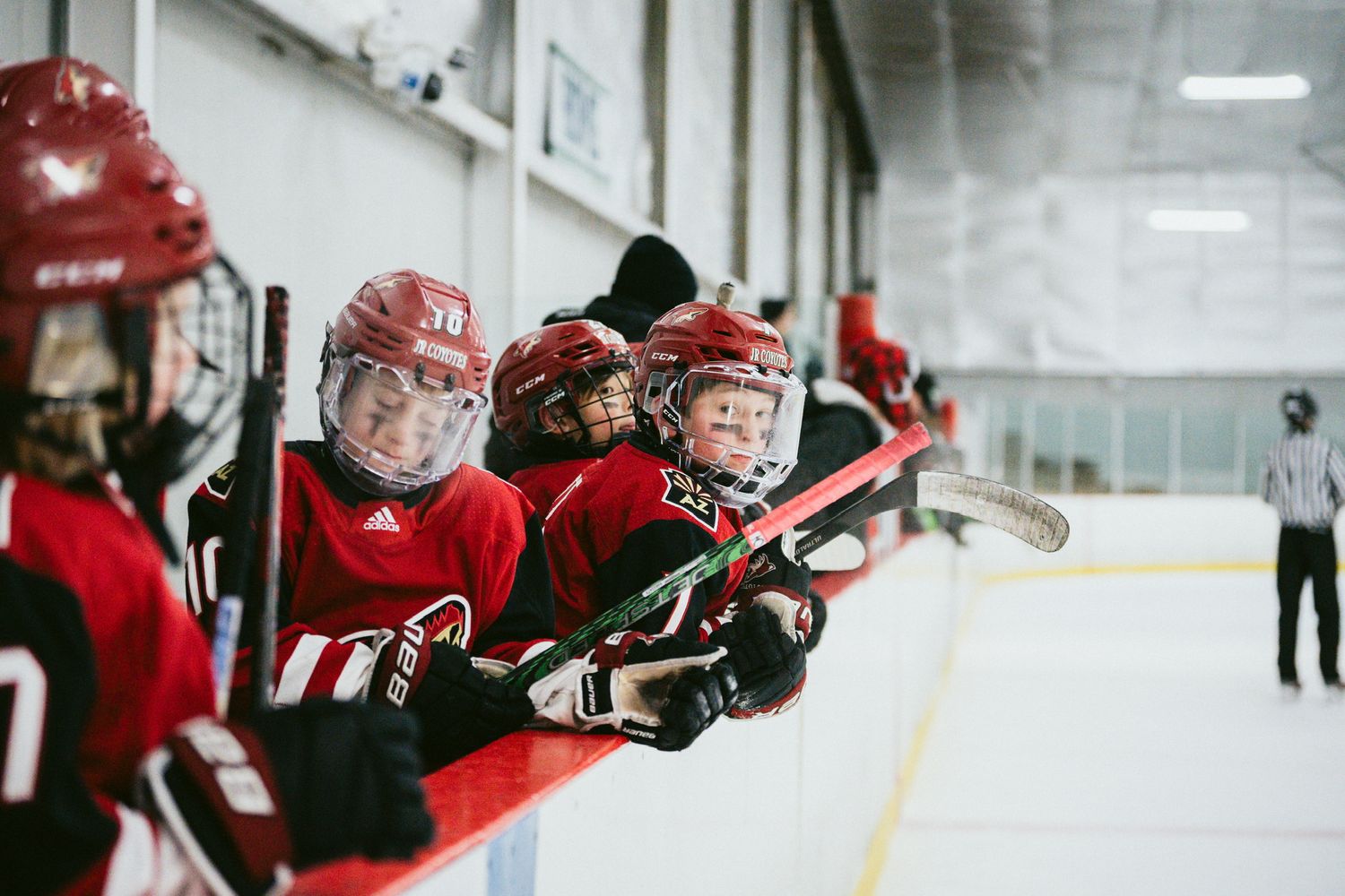 Young hockey players in red jerseys practice skating drills on an indoor ice rink.