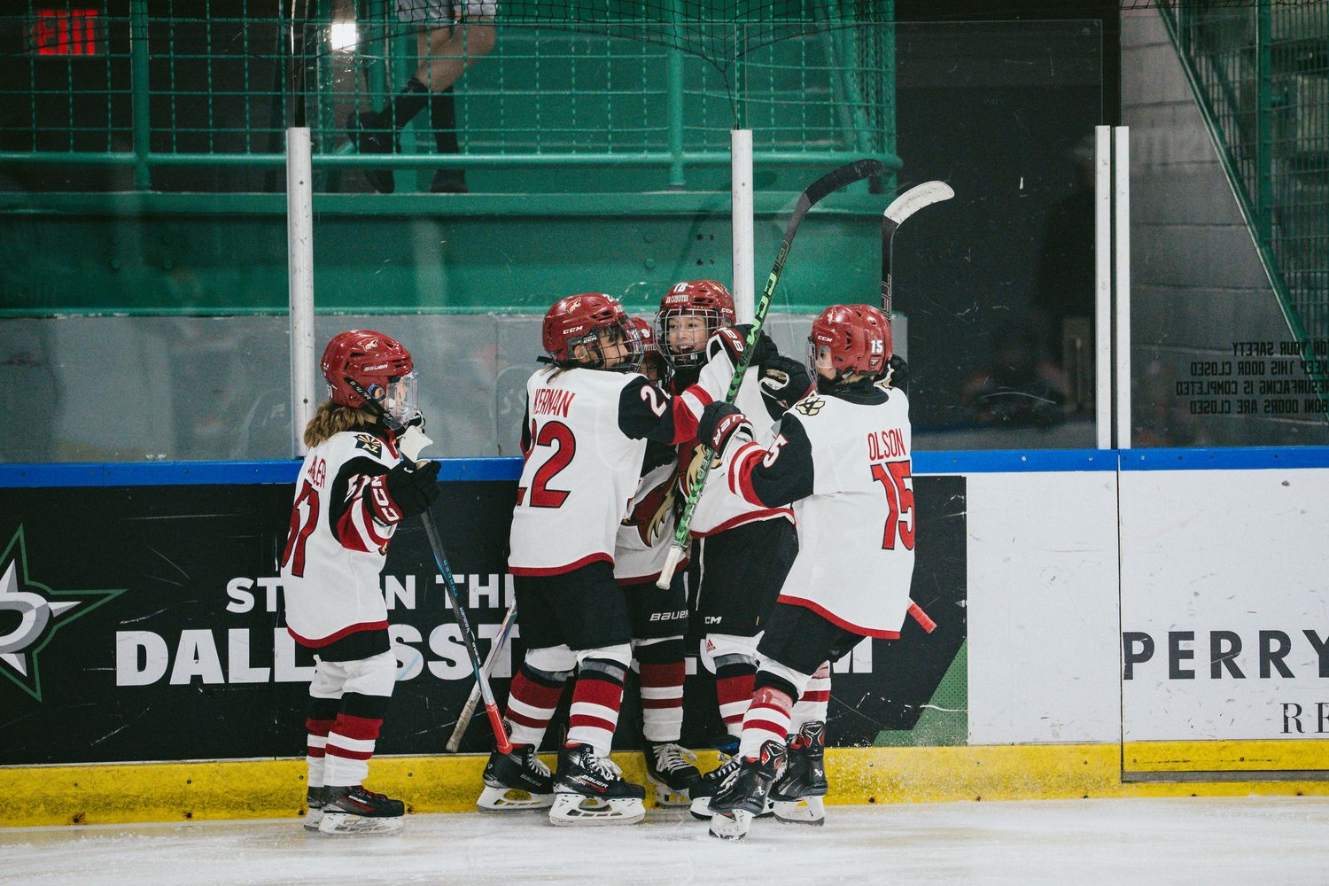 Youth hockey players practicing drills on ice with arena advertising boards visible.