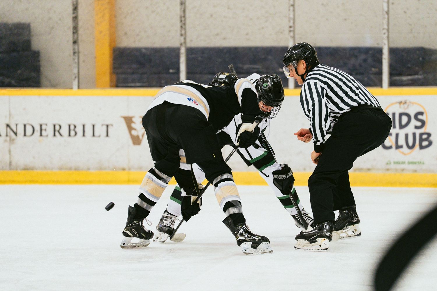 Two hockey players face off at center ice with a referee dropping the puck during an indoor hockey game.