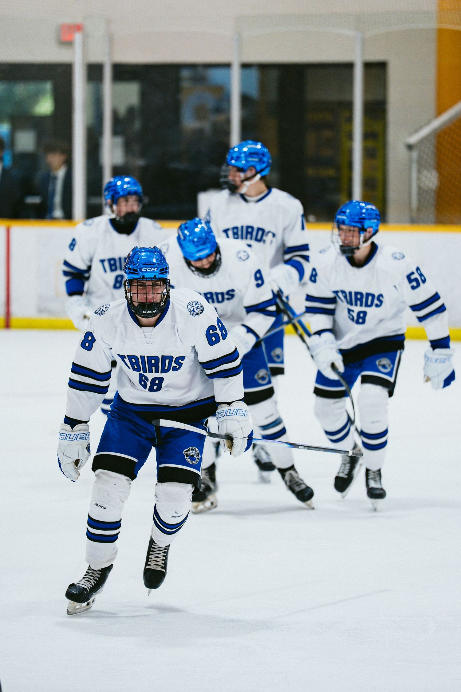 Ice hockey team in white and blue Thunderbirds uniforms skate in formation during a game warmup.