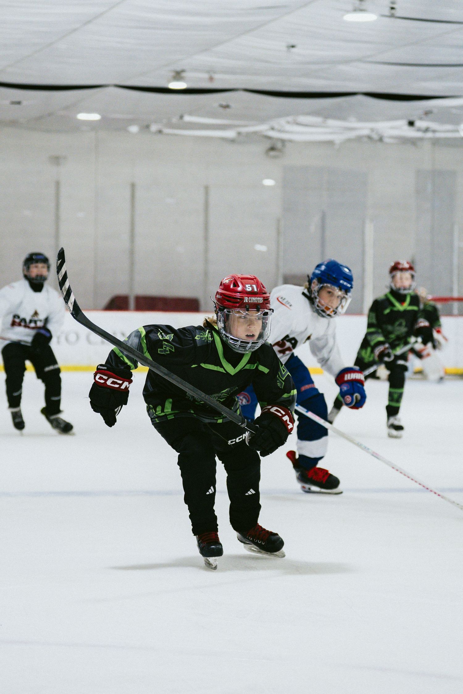 Young ice hockey player in red helmet leads skating drill during youth hockey practice at indoor rink.