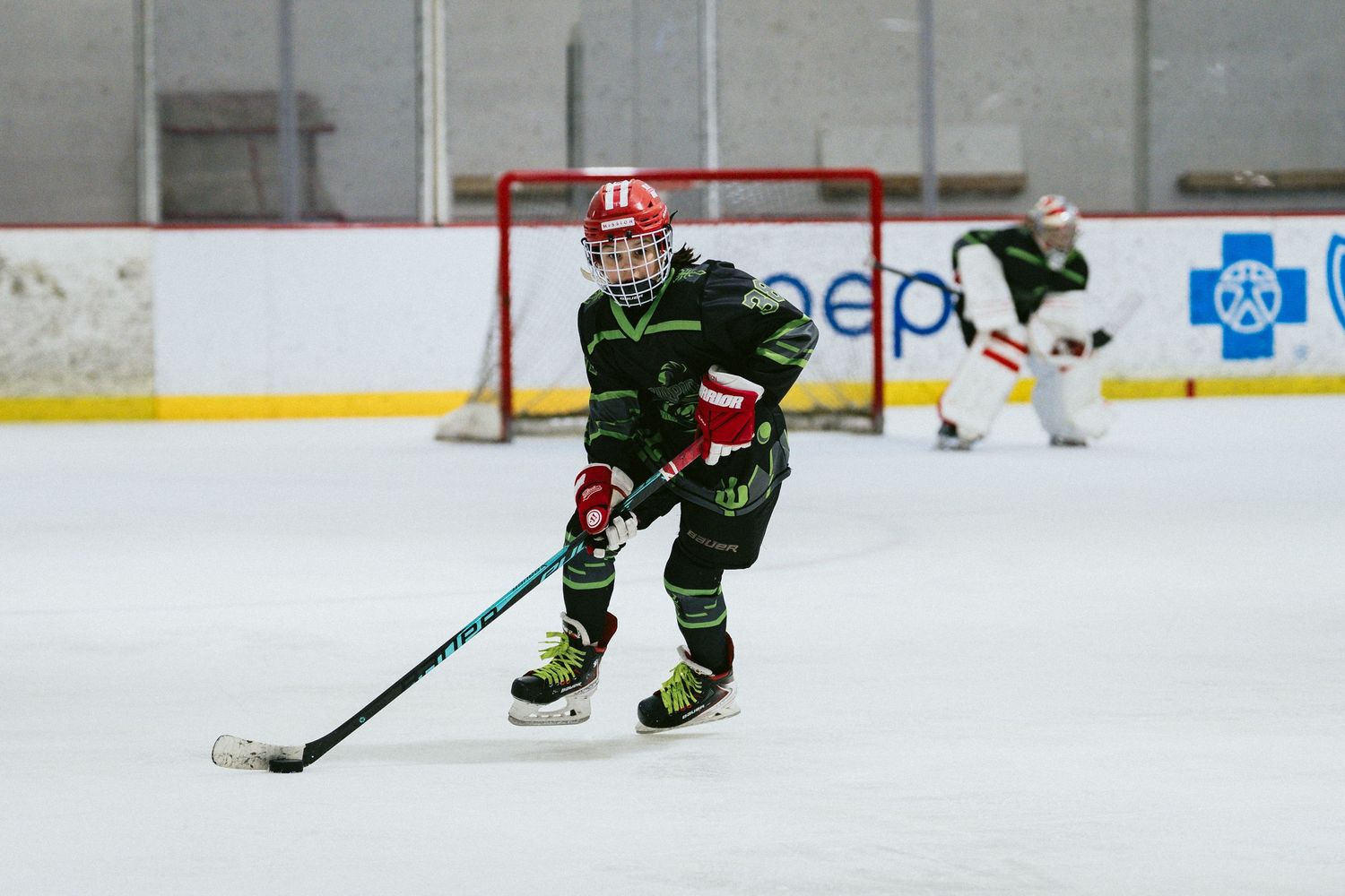 Youth hockey player in black green uniform skating with puck during indoor ice hockey game.