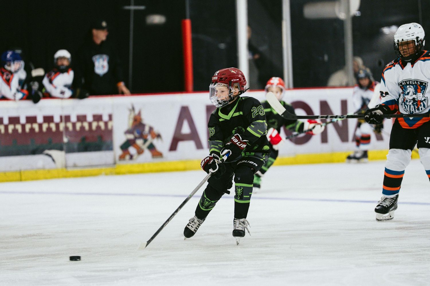 Young hockey player in black and green uniform skating with puck during youth ice hockey game.