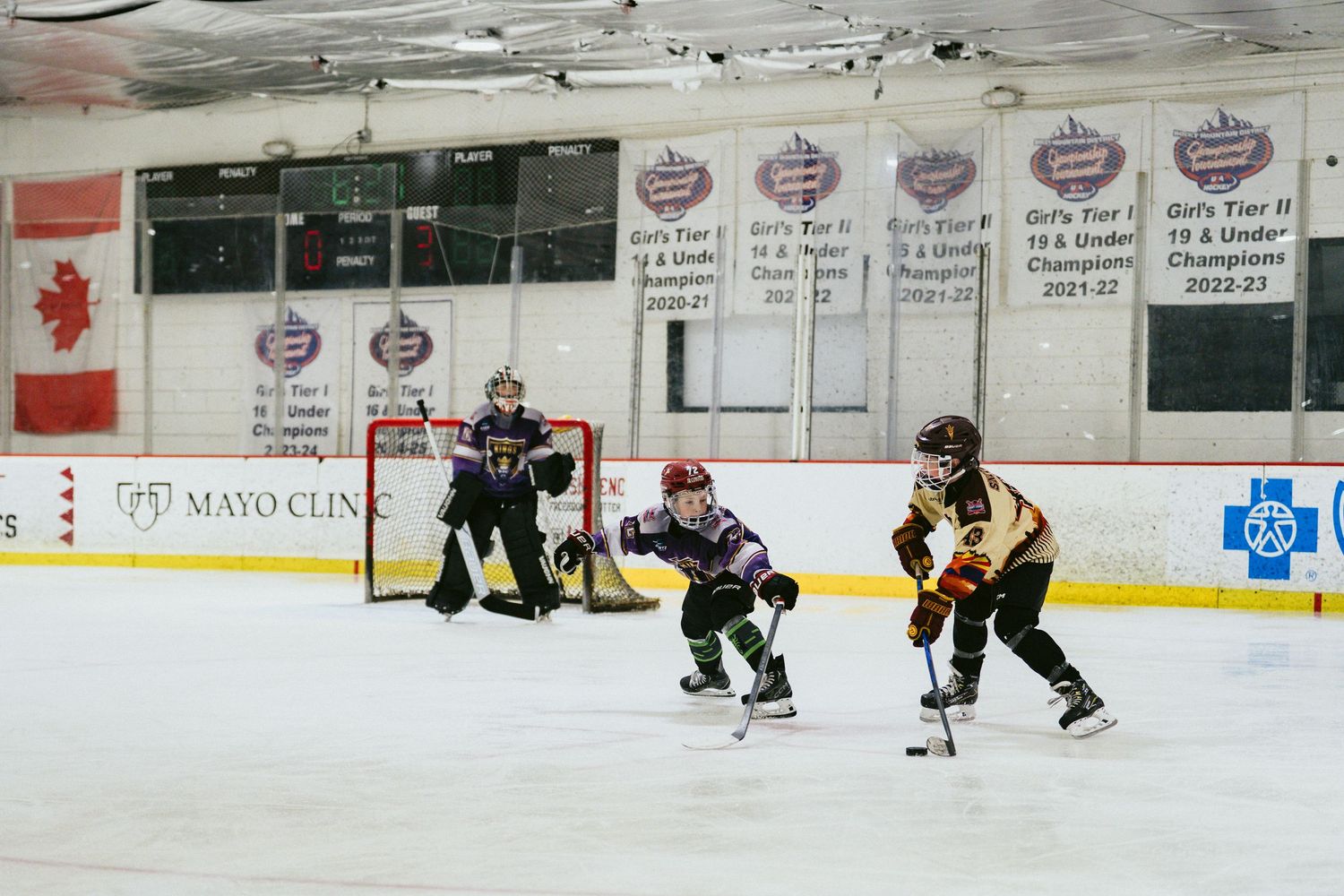Young girls play ice hockey near the goal during a youth tournament at an indoor rink.
