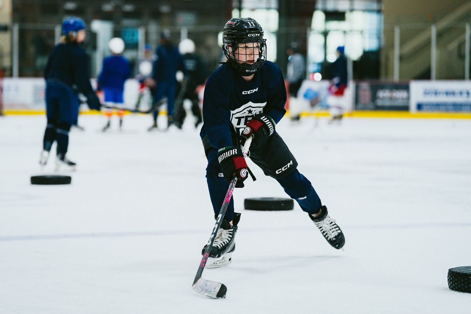 Young hockey player in navy TPH jersey skates hard on the ice during a drill at indoor hockey practice.