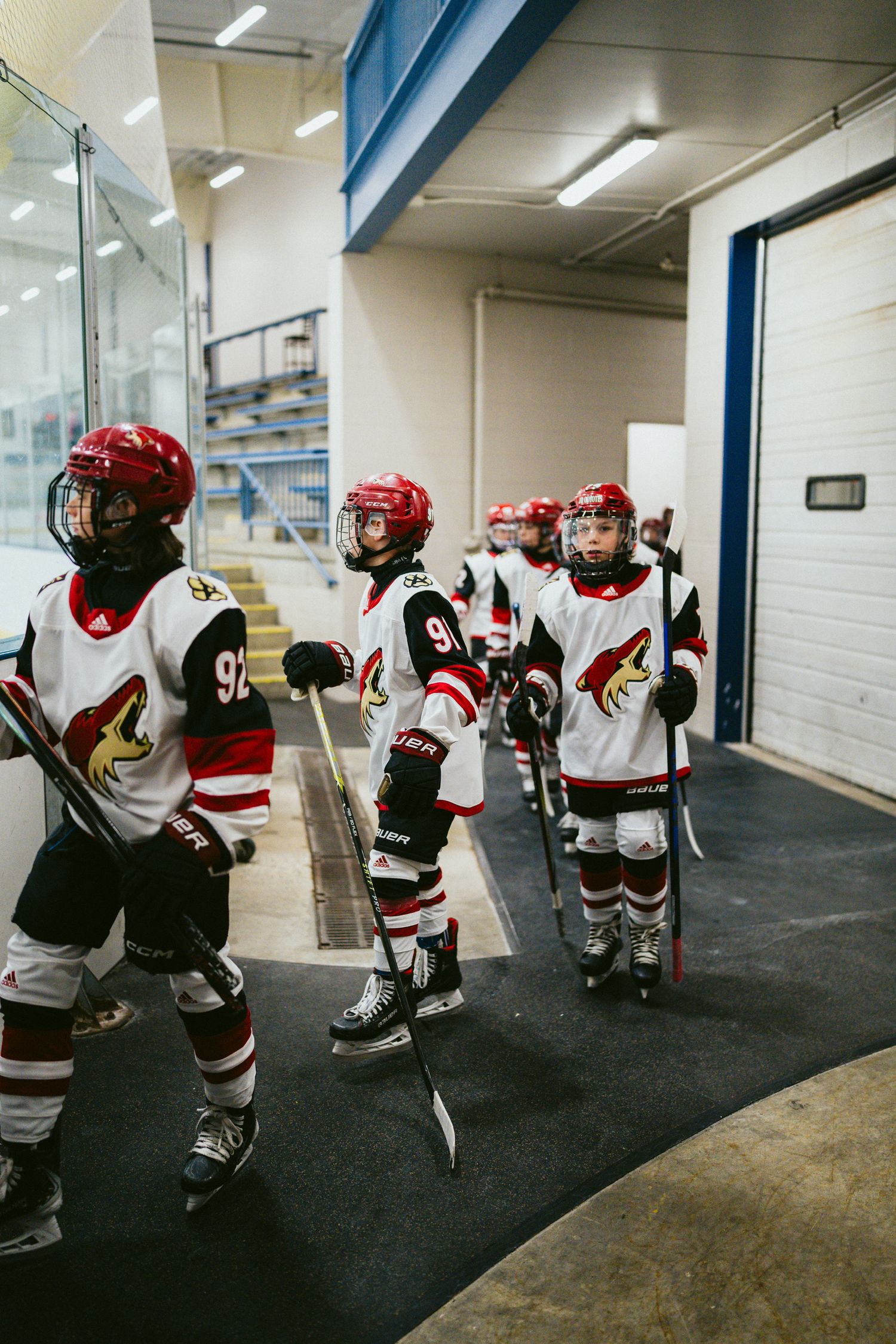 Youth hockey team lined up in a hallway wearing red and white jerseys before a game.