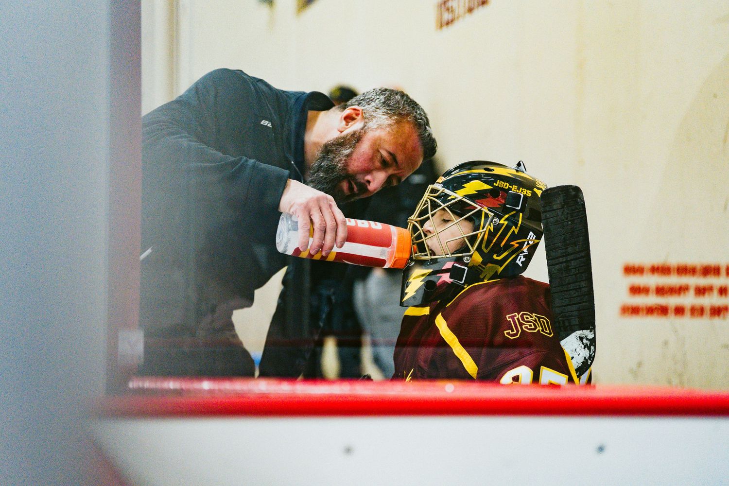 Youth hockey player in brown jersey skating near boards during game action.