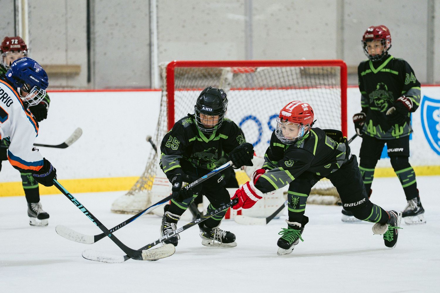 Young hockey players in black uniforms compete near the goal during a youth ice hockey game.