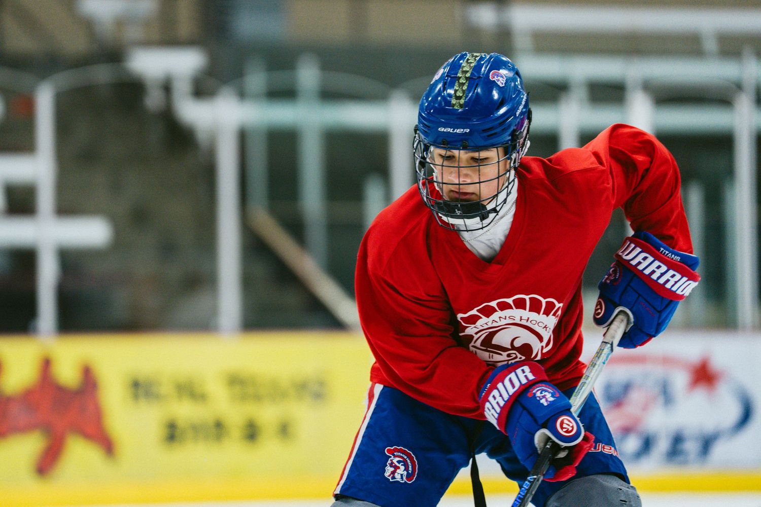 Young hockey player in red jersey and blue helmet aggressively skates with stick during indoor practice.