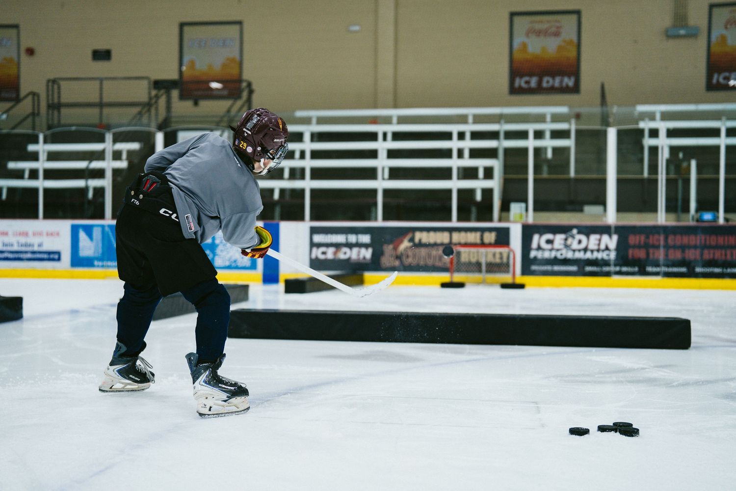 Hockey player practicing shots on ice at Ice Den arena during a training session.