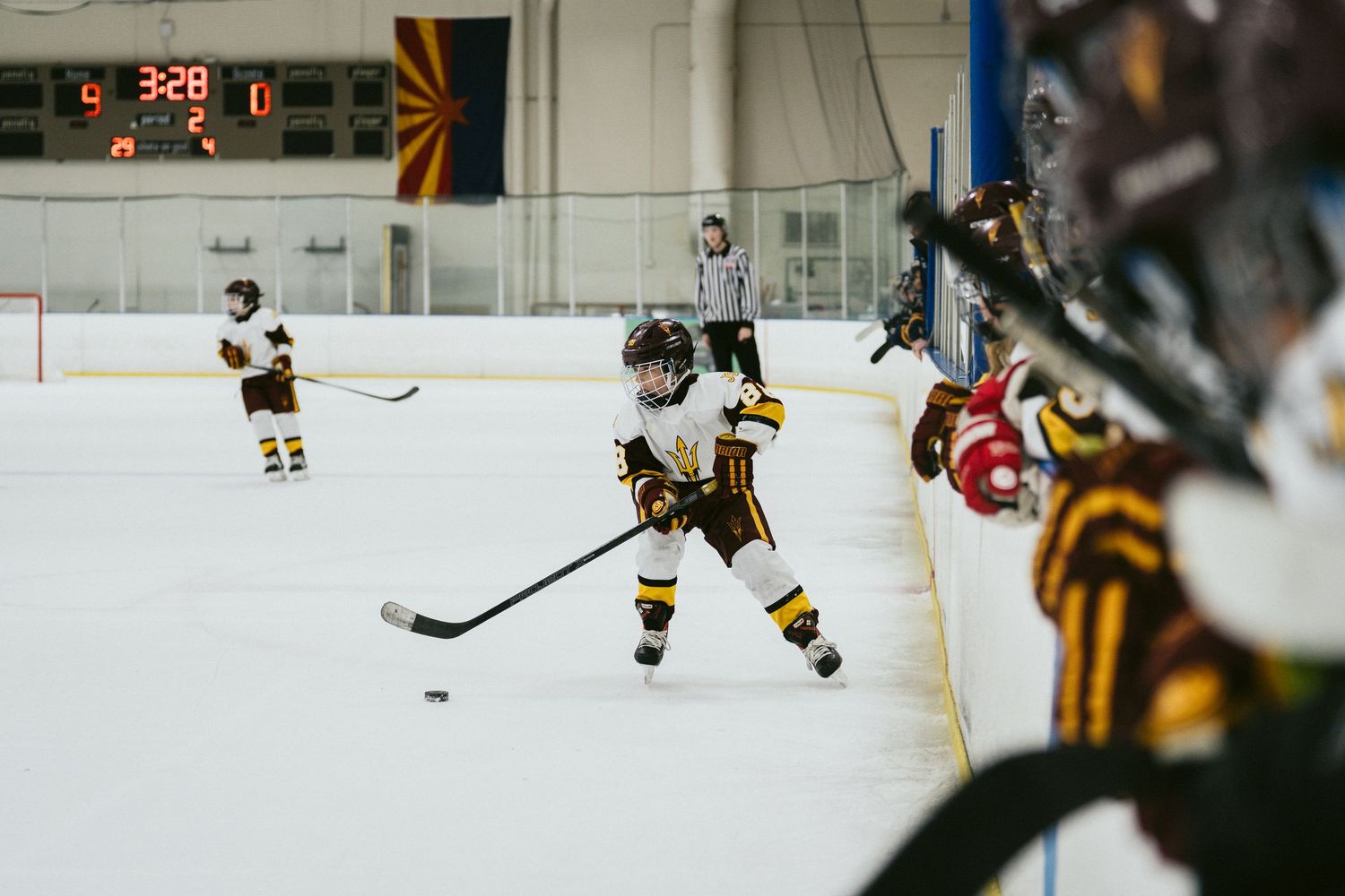 Young youth hockey player in gold uniform skates toward the puck during an indoor ice hockey game.