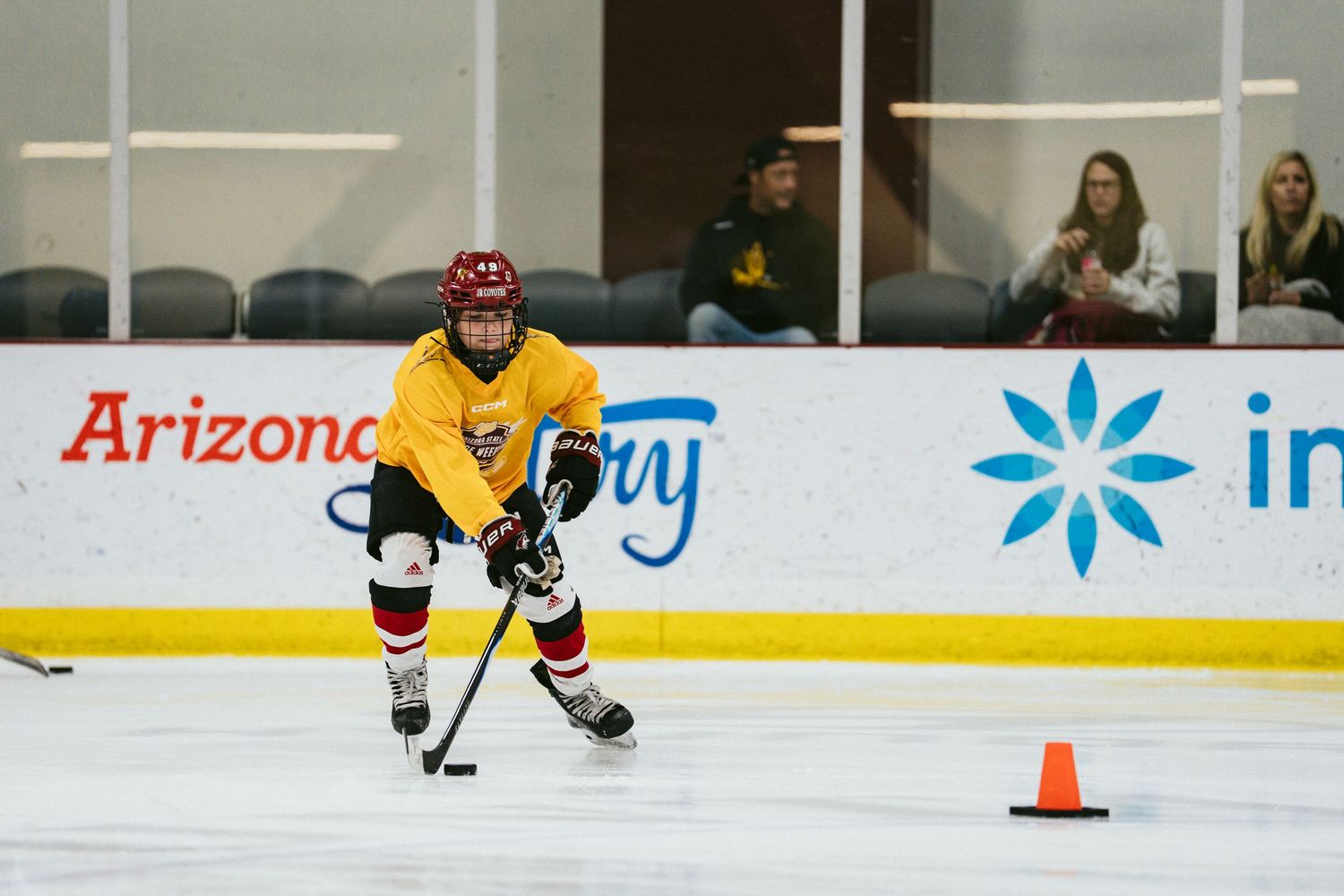 Youth hockey player in yellow jersey skating with puck past cone on Arizona rink.