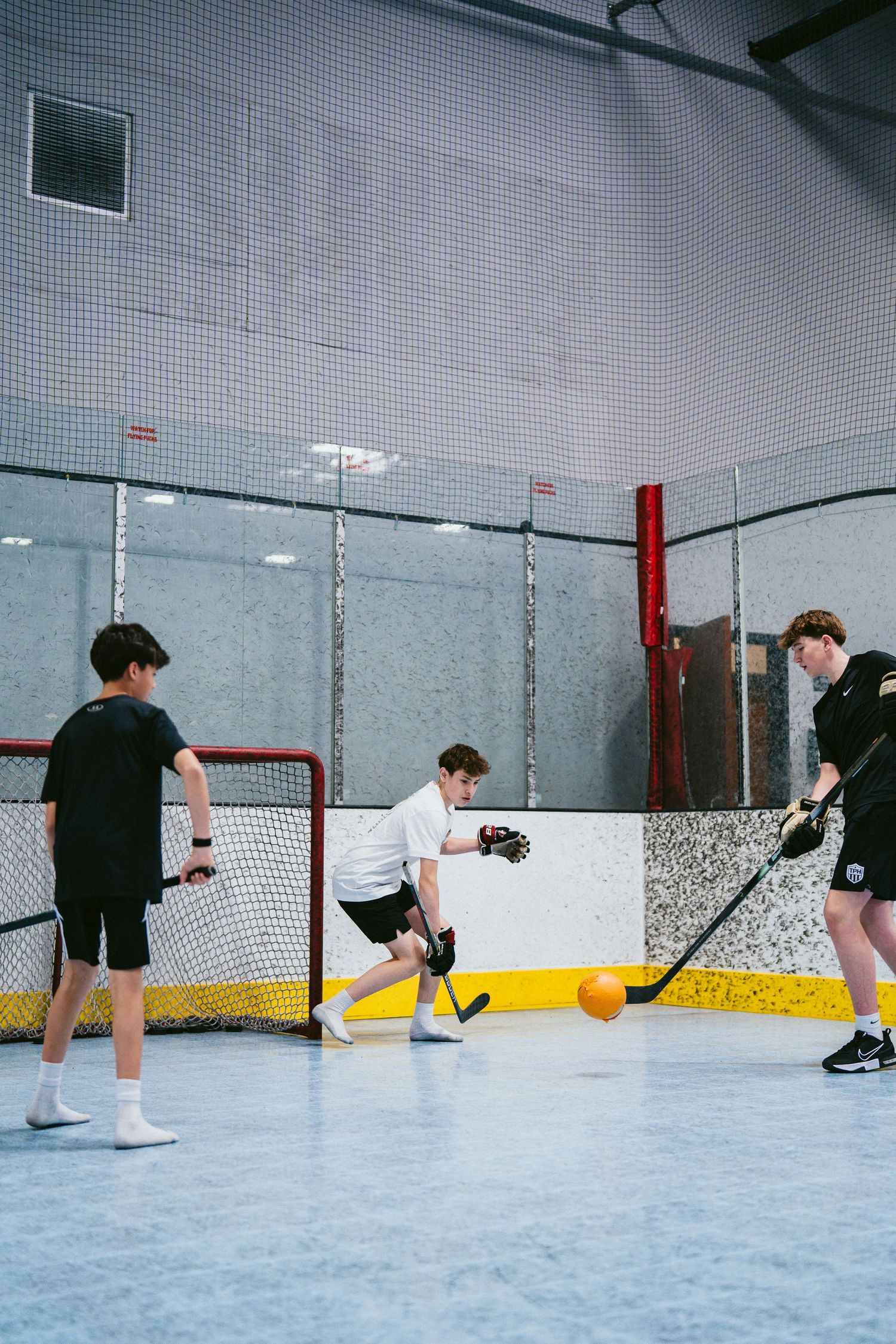 Three young players practicing floor hockey with a goal net in an indoor rink.