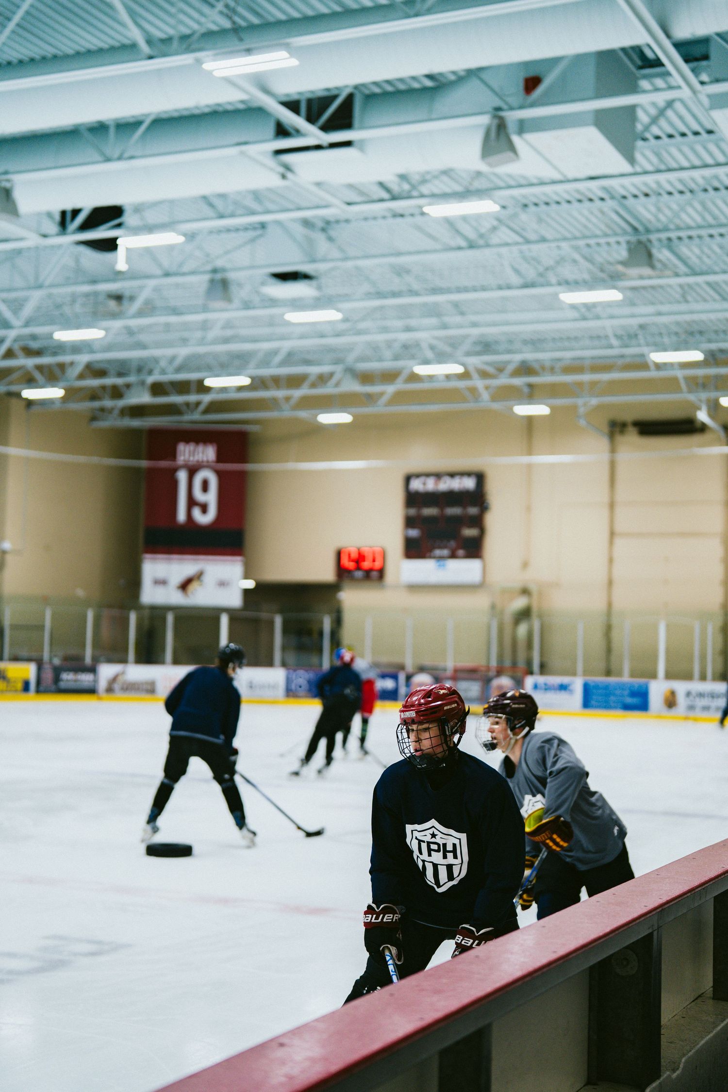 Young hockey player in TPH jersey stands at rink boards during indoor ice practice.