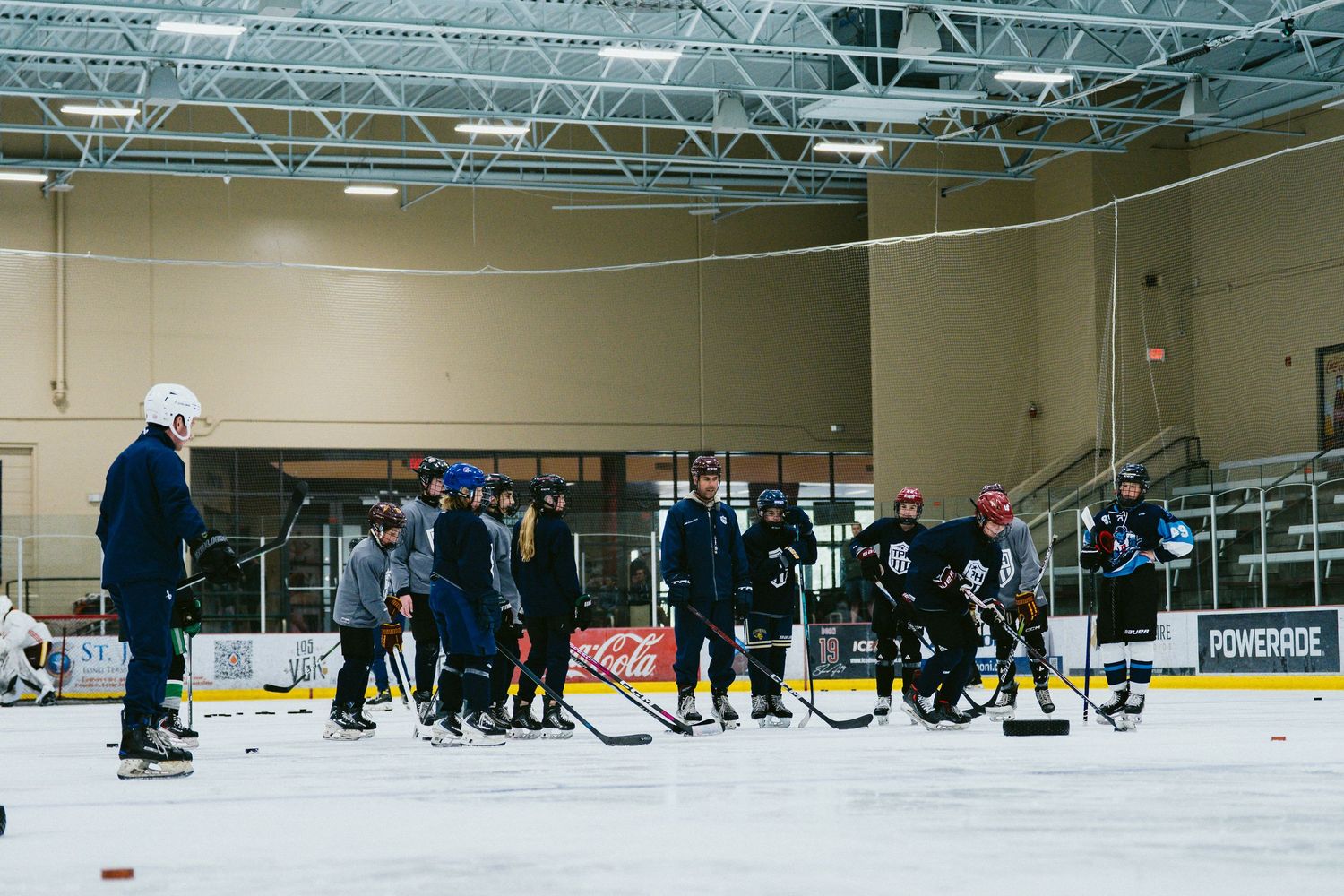 Hockey players and coaches gather on an indoor ice rink during a practice session in a sports arena.