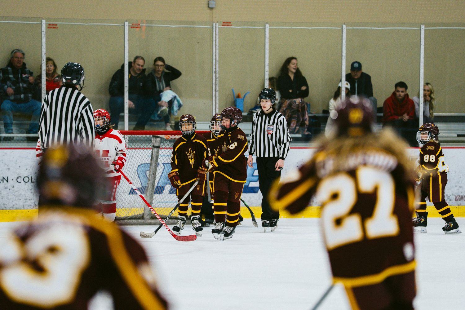 Wide angle view of a youth hockey game with spectators watching from the sidelines.