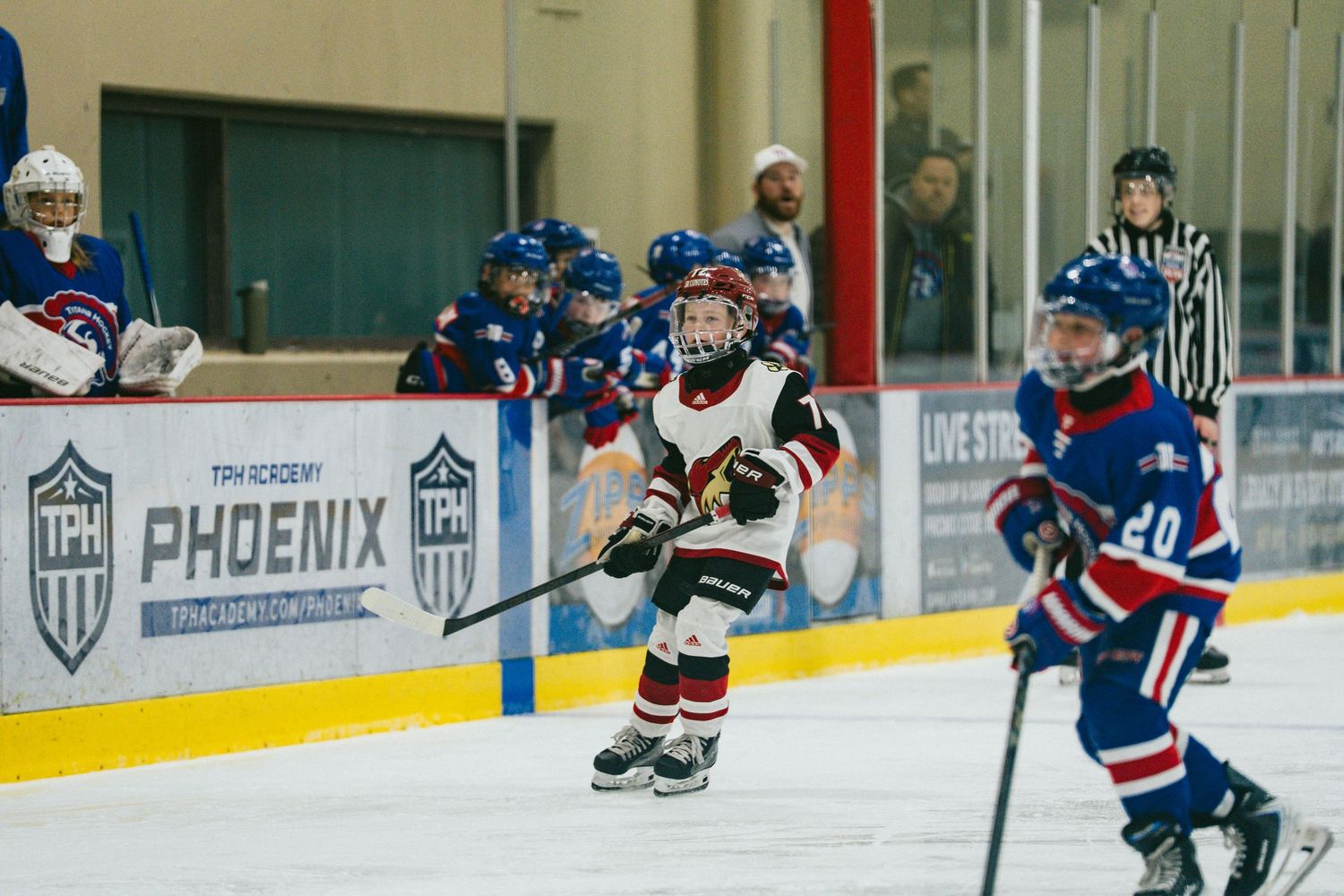 Youth hockey players from opposing teams battle for puck possession on the ice.