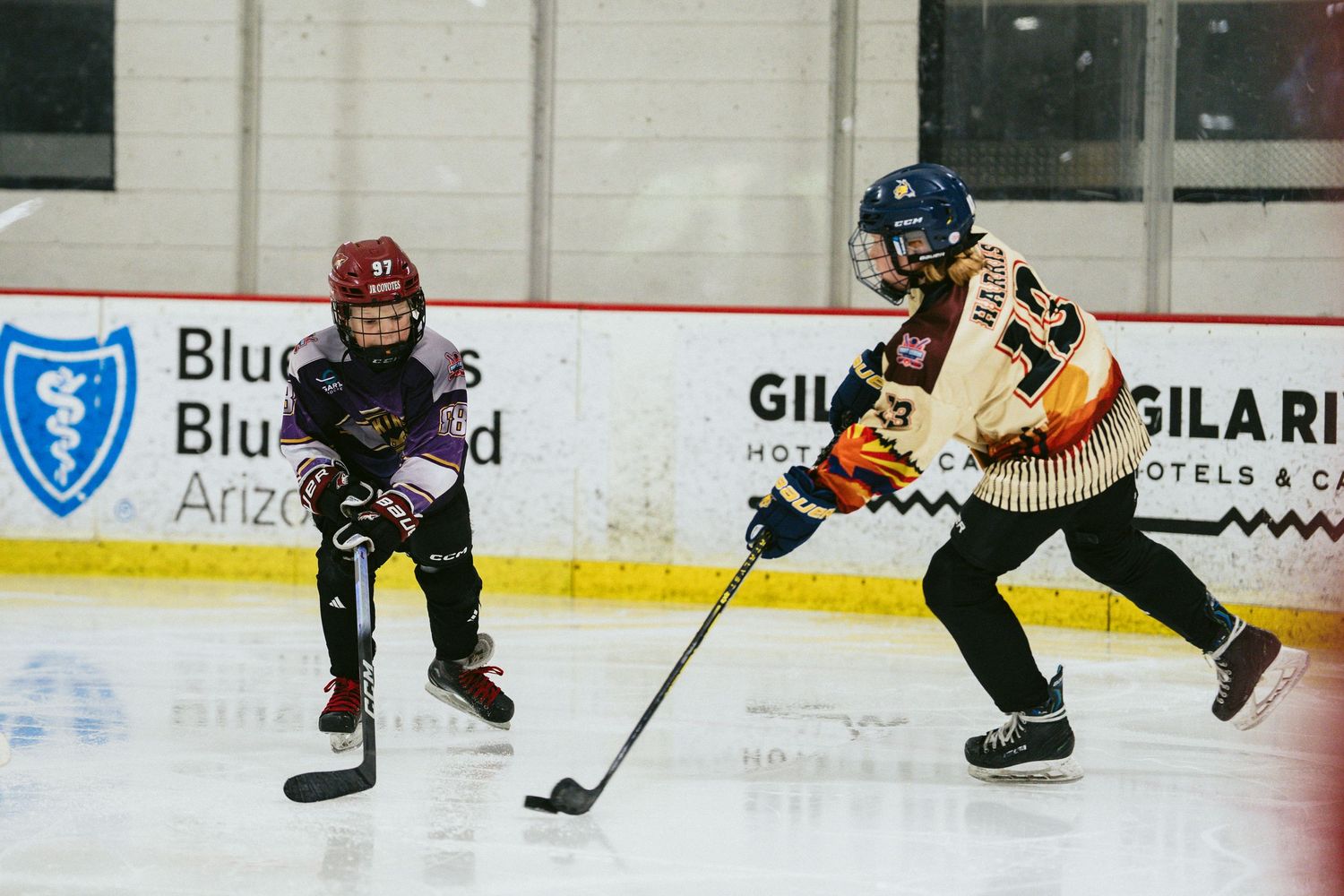 Two young hockey players battle for the puck during a youth ice hockey game indoors.
