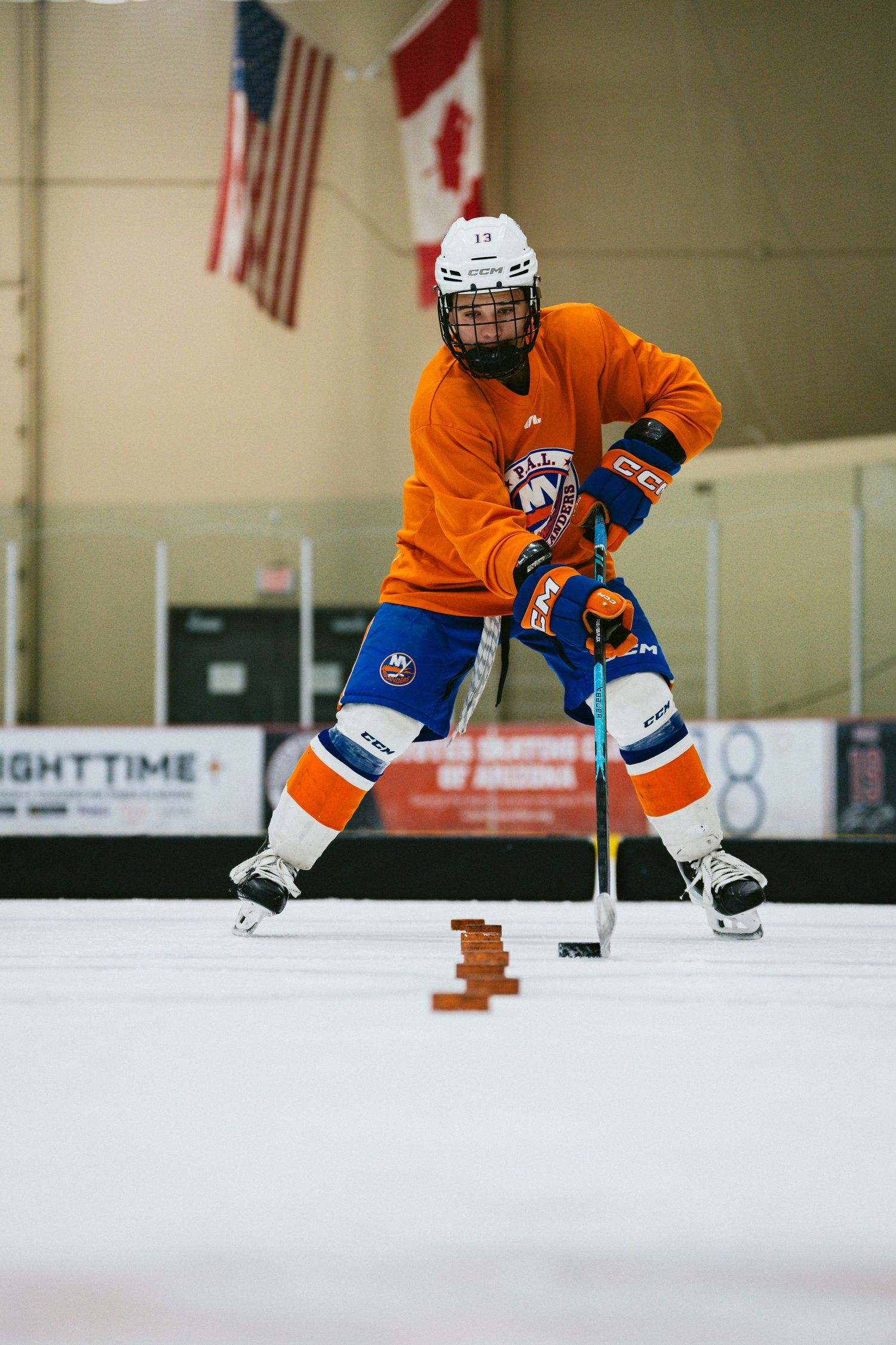 Hockey player in orange New York Islanders jersey handles the puck during an indoor ice rink training drill.