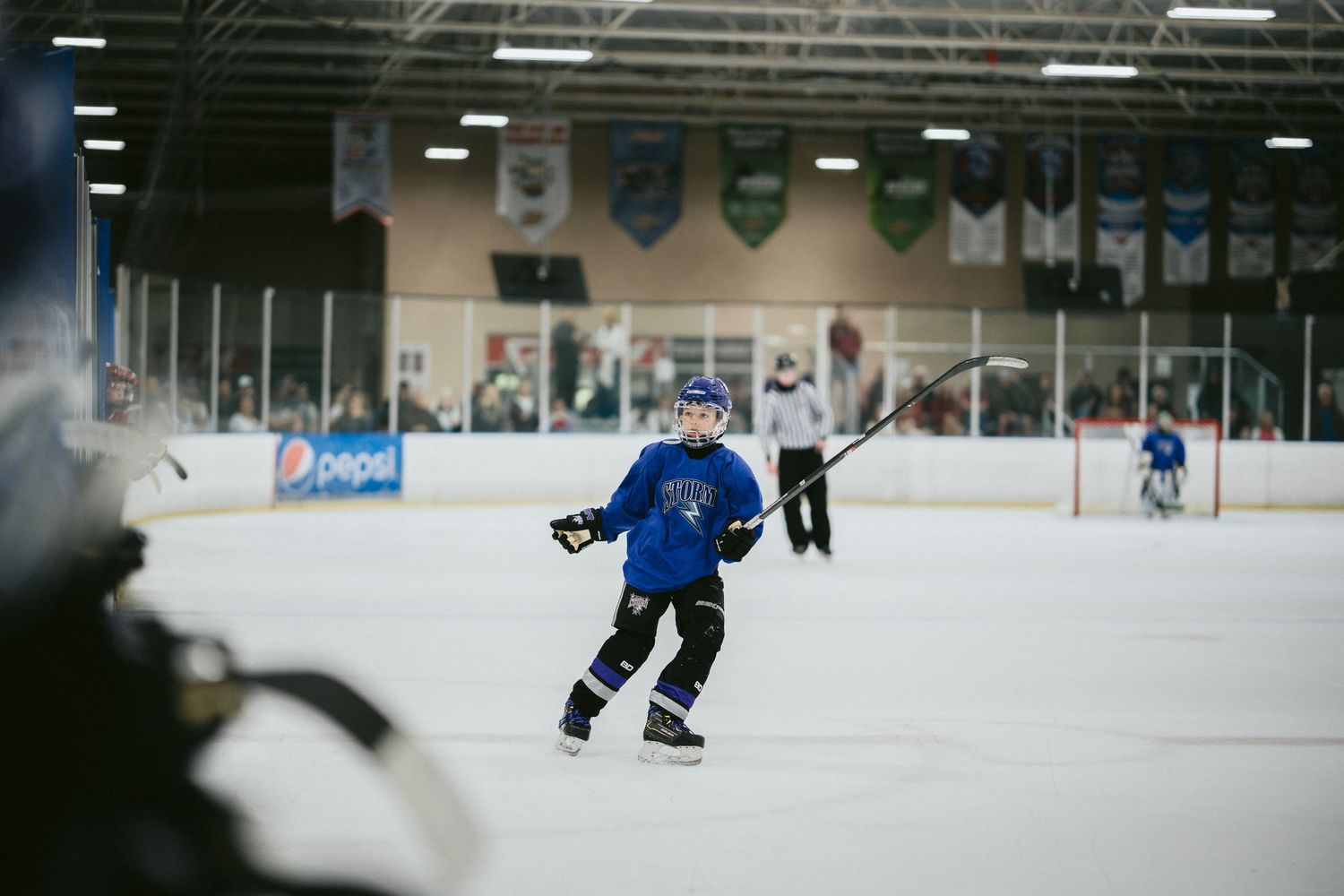 Young hockey player in blue jersey skating on indoor ice rink during practice session.